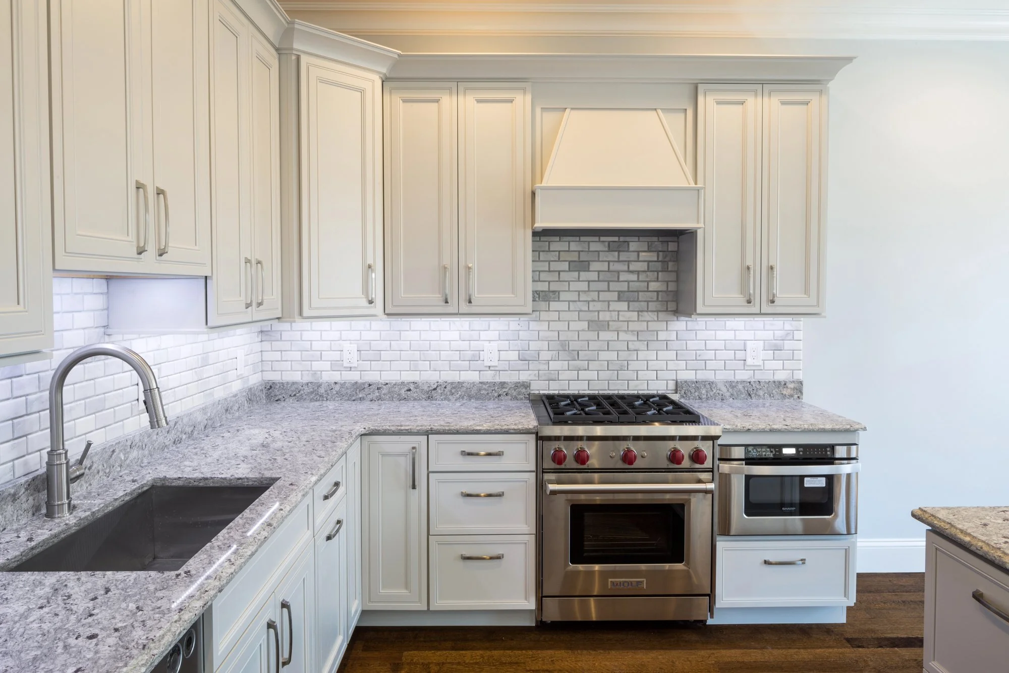 Modern kitchen with white cabinets, granite countertops, white subway tile backsplash, and stainless steel appliances including a stove and oven.