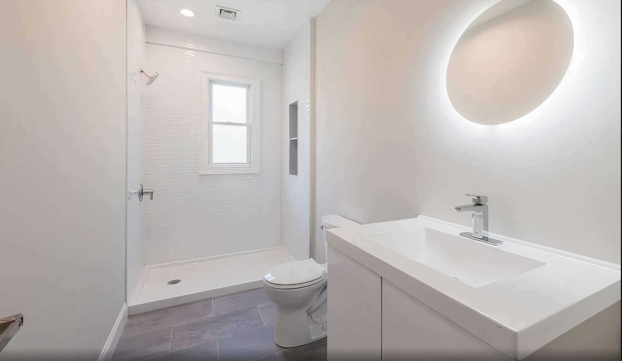 A modern, white bathroom featuring a window, a shower area, a toilet, and a vanity with a rectangular sink and mirror with backlighting.