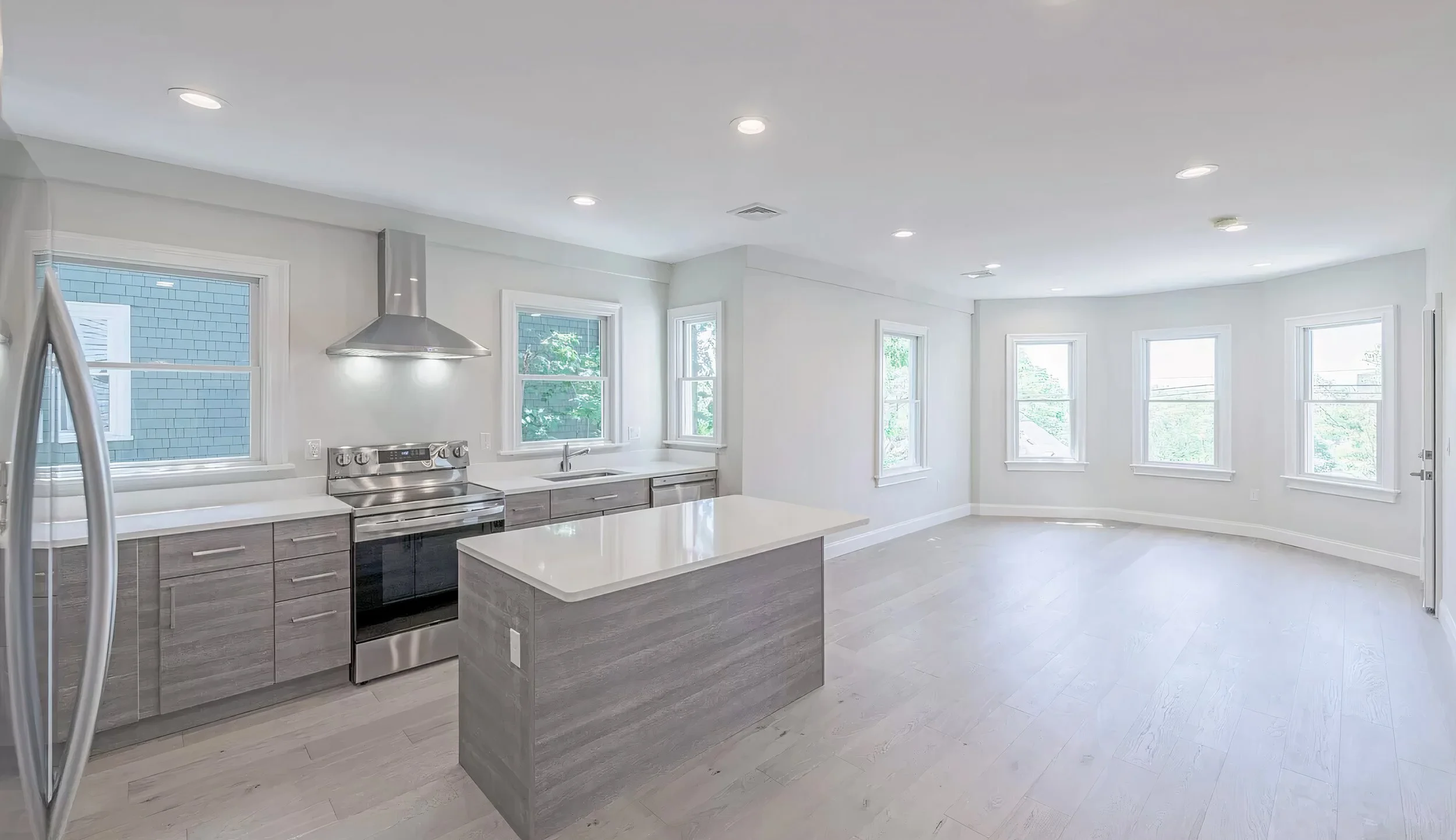 Bright, modern kitchen with white walls, multiple windows, stainless steel appliances, and light-colored wooden cabinets.