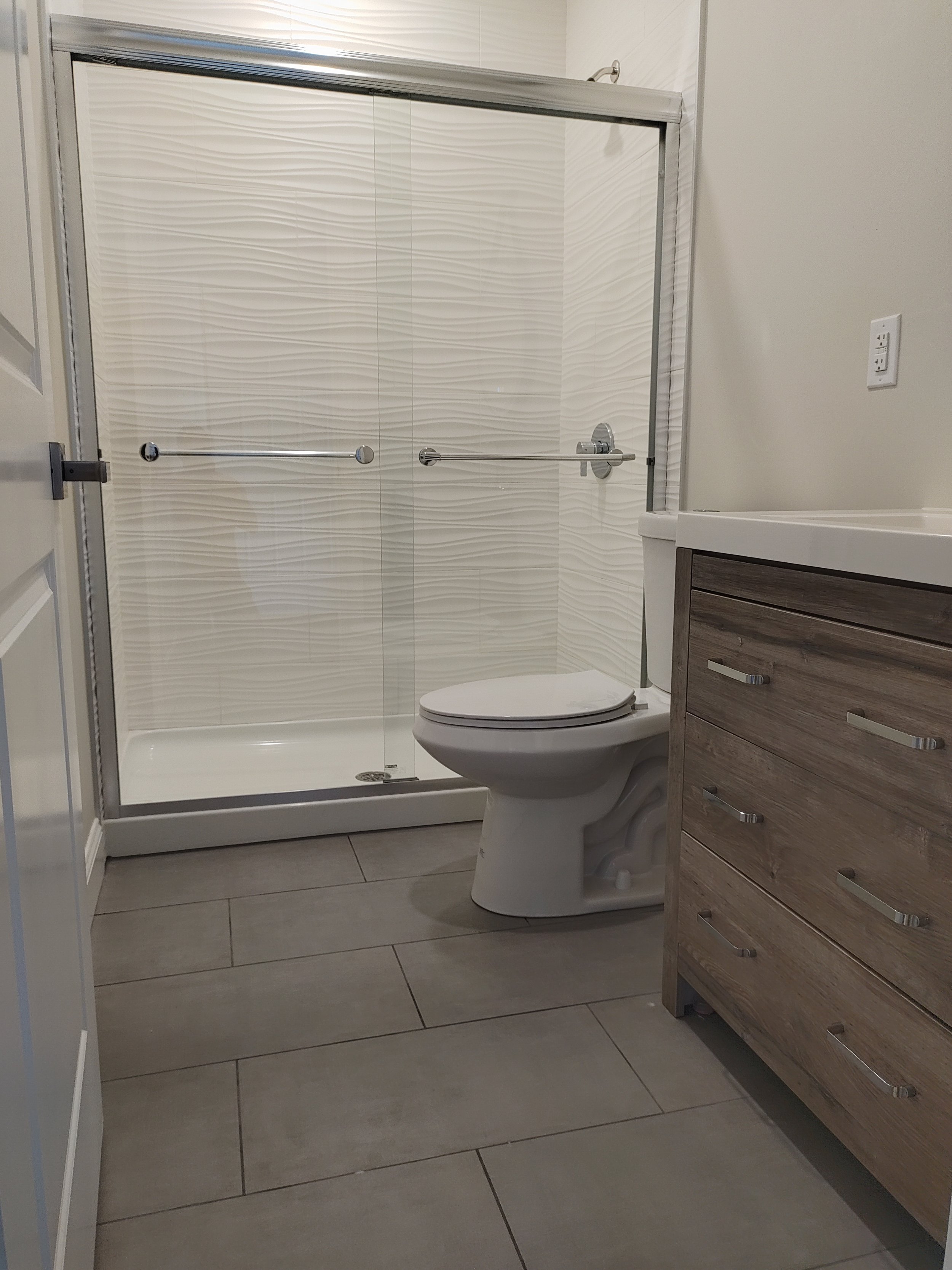 A modern bathroom with a glass shower enclosure, a toilet, and a wooden vanity with a light-colored countertop.