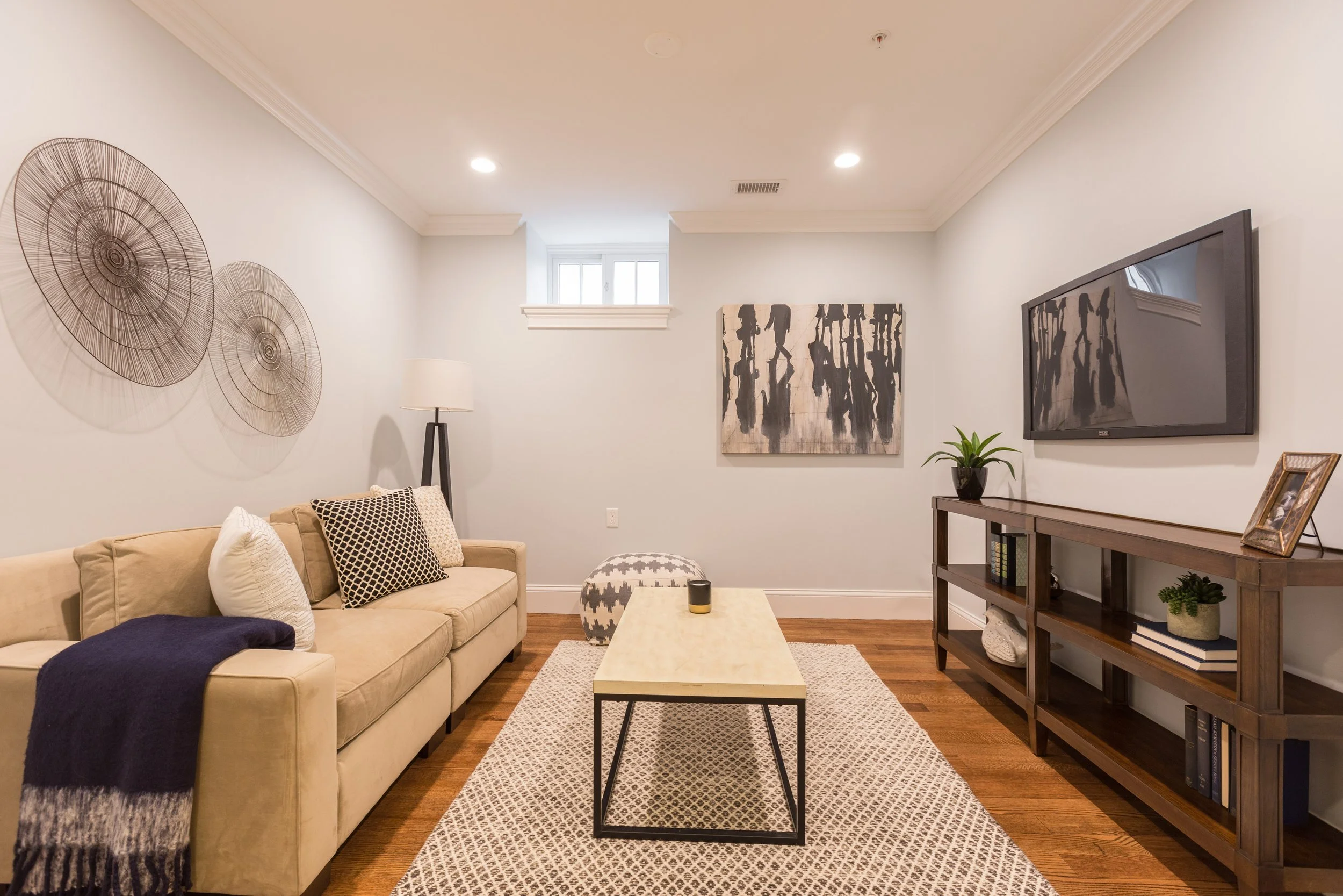 Living room with beige sofa, black and white pillows, coffee table, wall art, potted plant, TV, and decorative shelving.