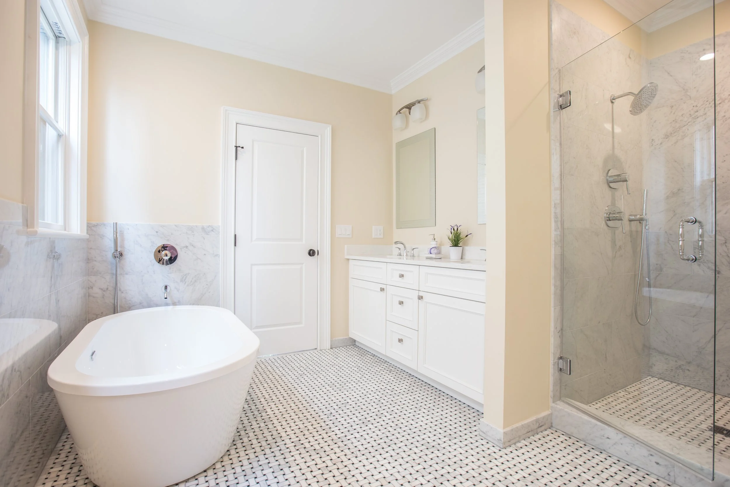 Bathroom with a free-standing bathtub, a vanity with a mirror, and a glass-enclosed shower with marble tiles.