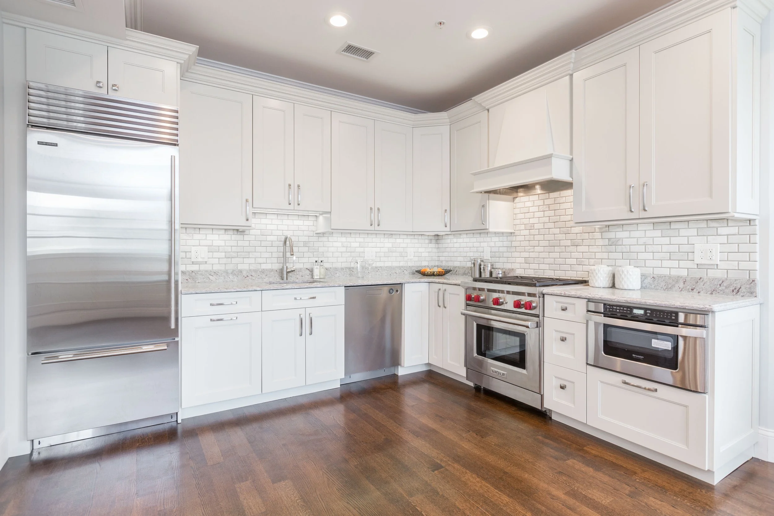 Modern kitchen with white cabinets, stainless steel appliances, a brick backsplash, and dark hardwood floors.
