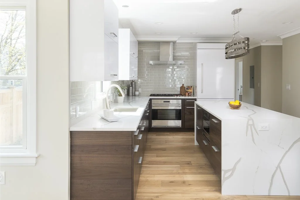 Modern kitchen with white and wooden cabinetry, white marble countertops, stainless steel appliances, and a hanging light fixture.
