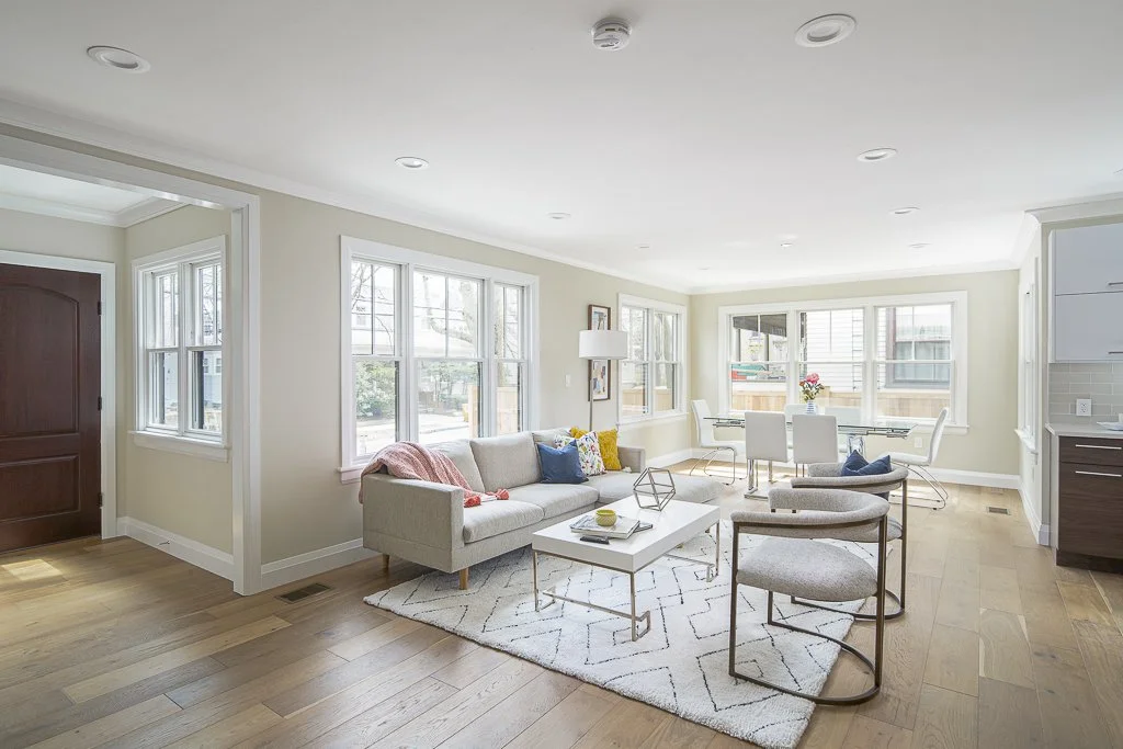 Bright living room with a beige sofa, two matching armchairs, white coffee table, and large windows letting in natural light.