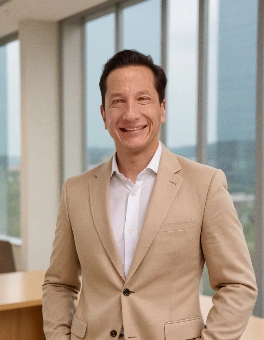 Hombre sonriendo en un entorno de oficina con ventanas grandes y vista del paisaje exterior.