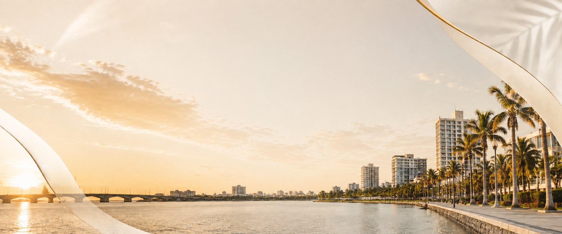 Vista de la bahía al atardecer con edificios altos, palmeras y un puente, en un ambiente tropical.
