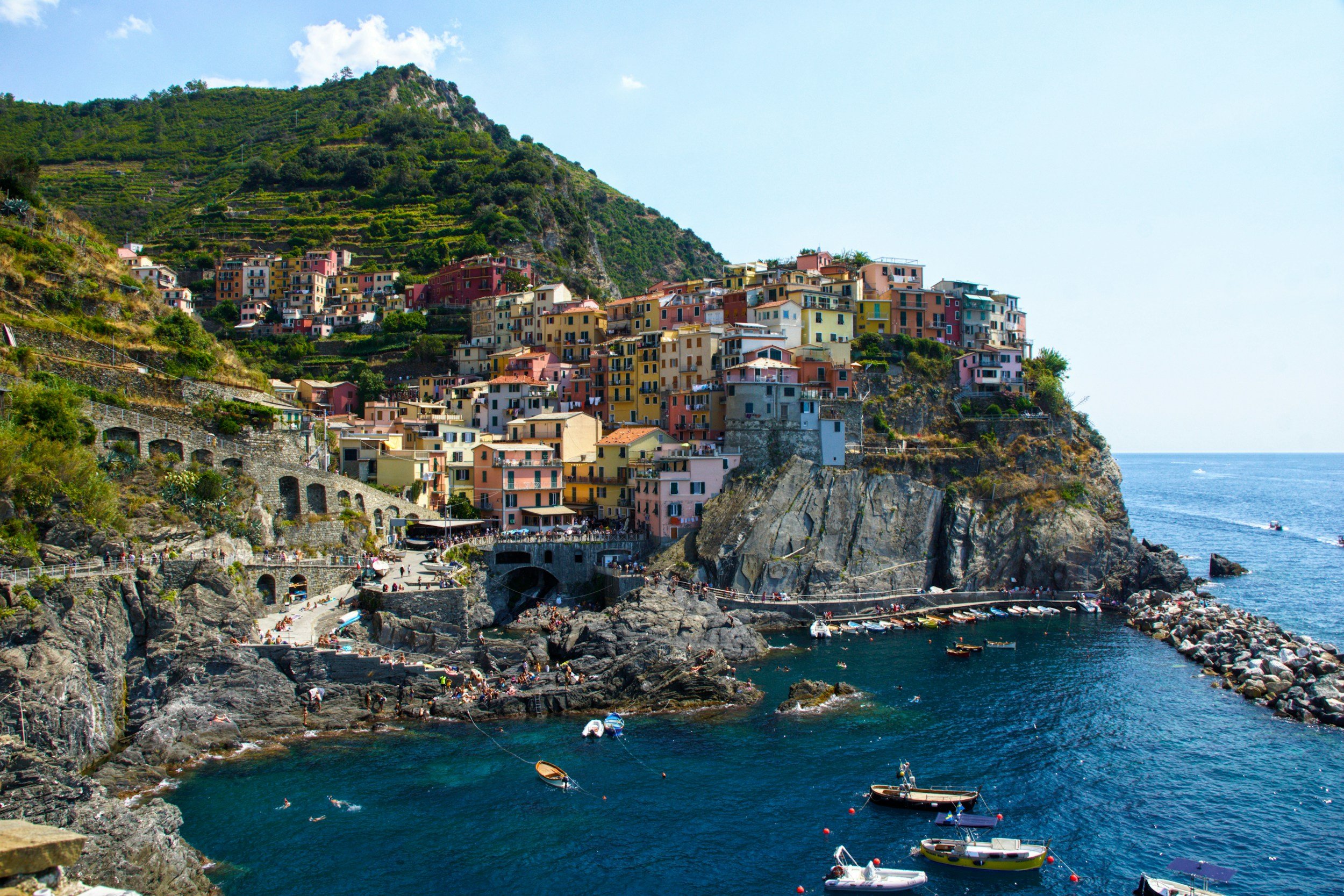 Colorful houses built on a steep hillside overlooking the Mediterranean Sea with boats docked along the rocky shore. Italy.