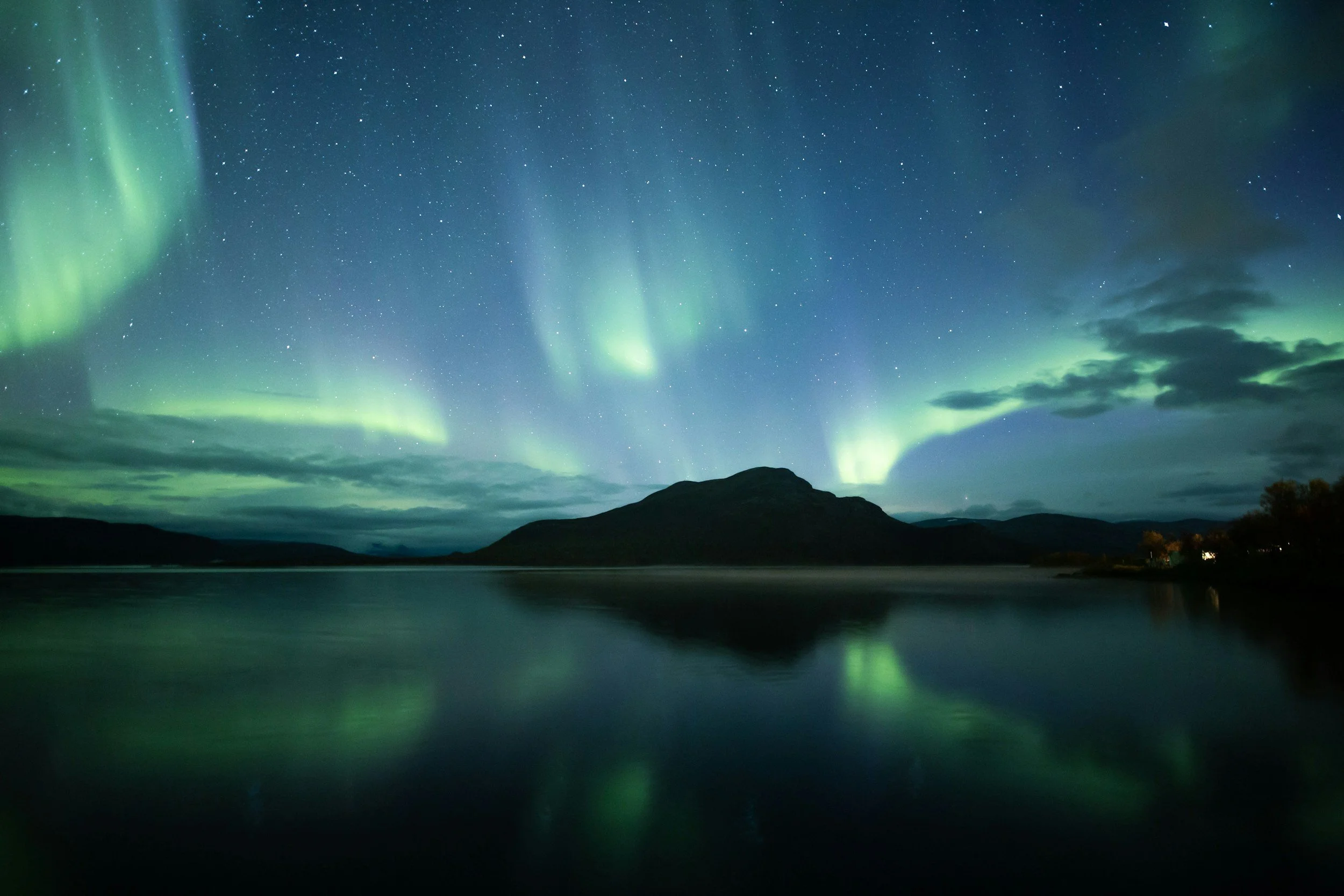 Northern Lights (aurora borealis) over a body of water at night with mountains in the background. Finland.