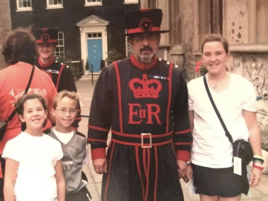 Group of children and adults, with a Beefeater in front of the Tower of London. Located in England.