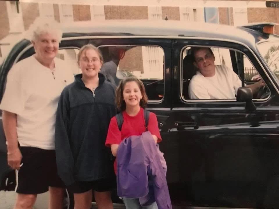 Older woman and two young girls in front of a black taxi cab in London, England, United Kingdom