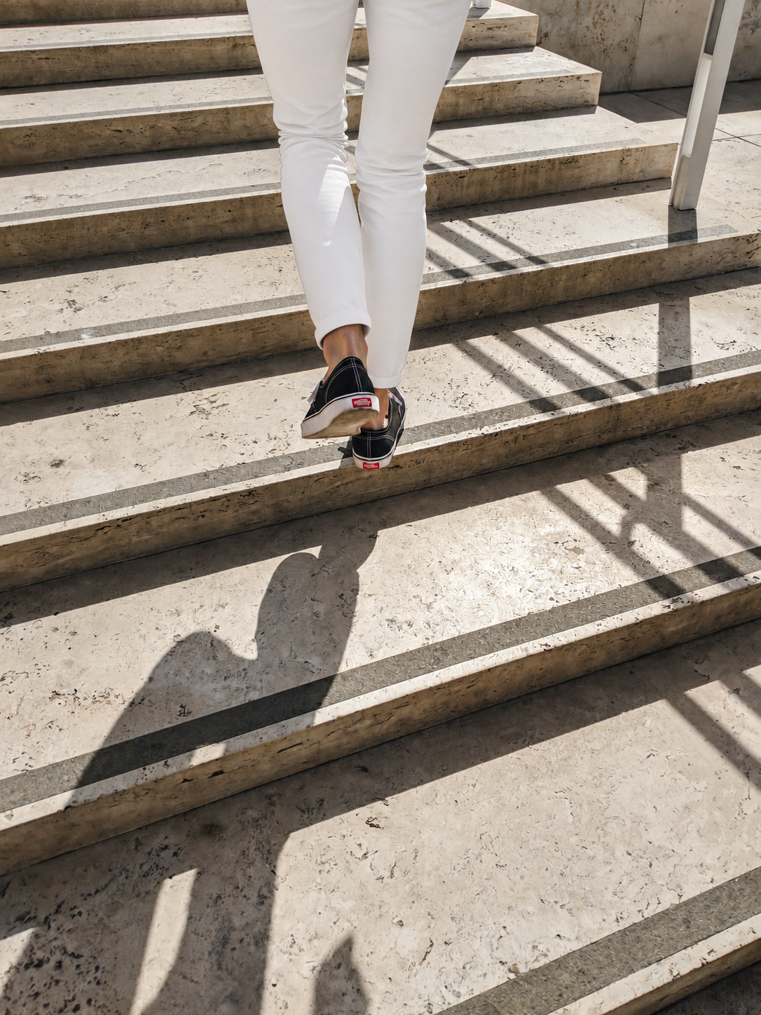 Woman in white pants and black sneakers climbing outdoor stone steps, taking the next step forward.