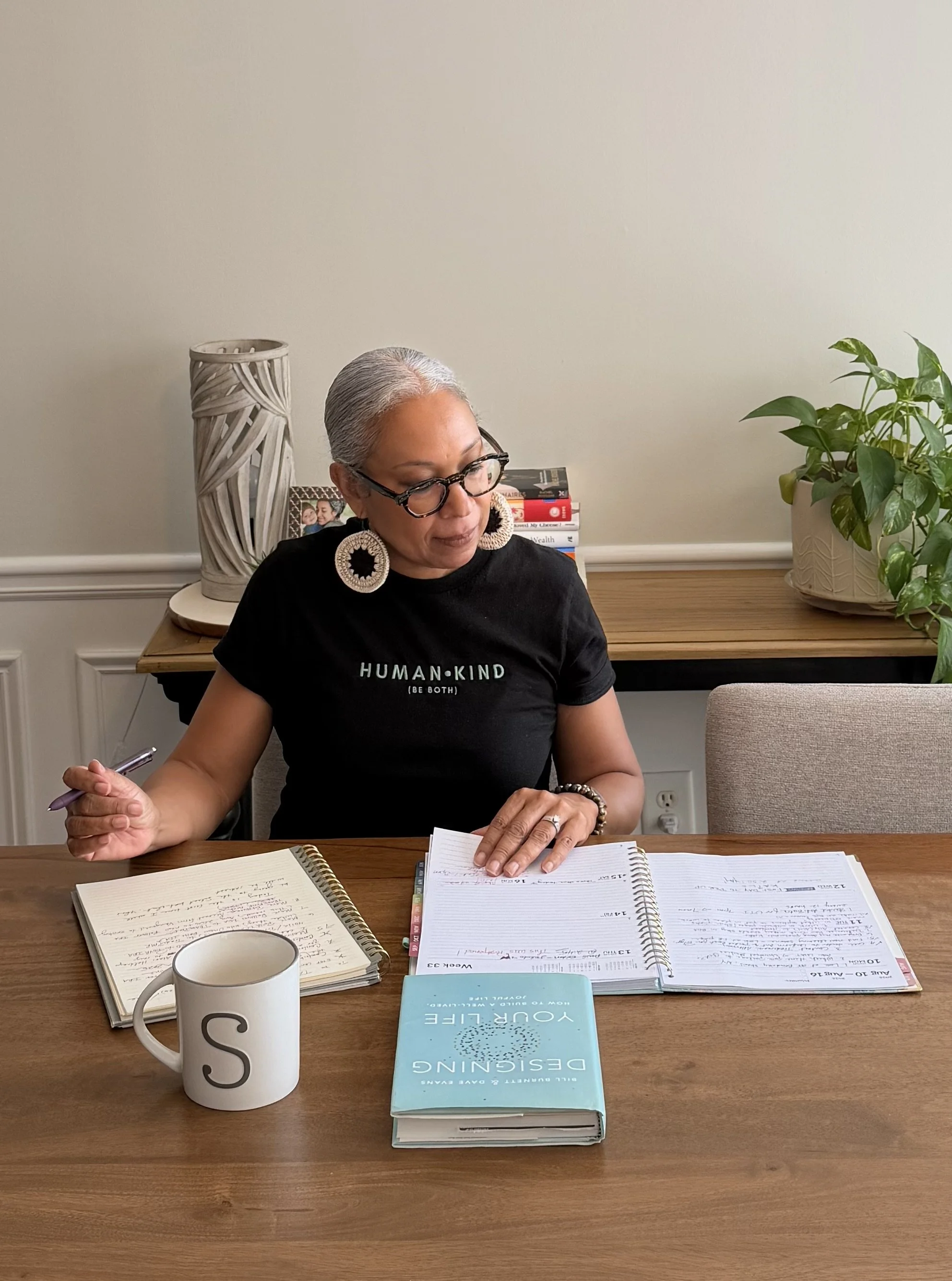 Woman with gray hair sitting at a table with notebooks, books, and a coffee mug.