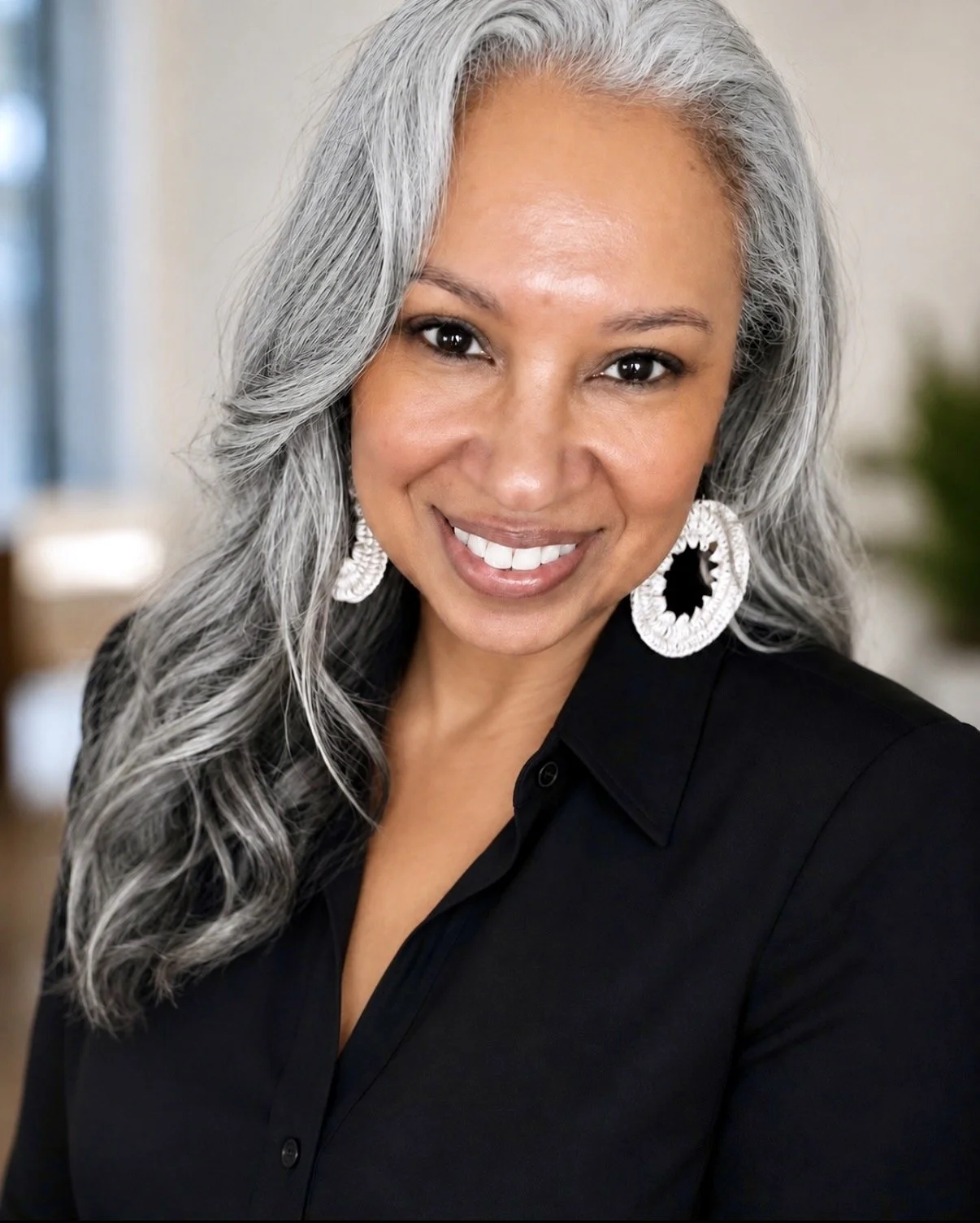 Smiling woman with long silver-gray hair, white statement earrings, and a black top.