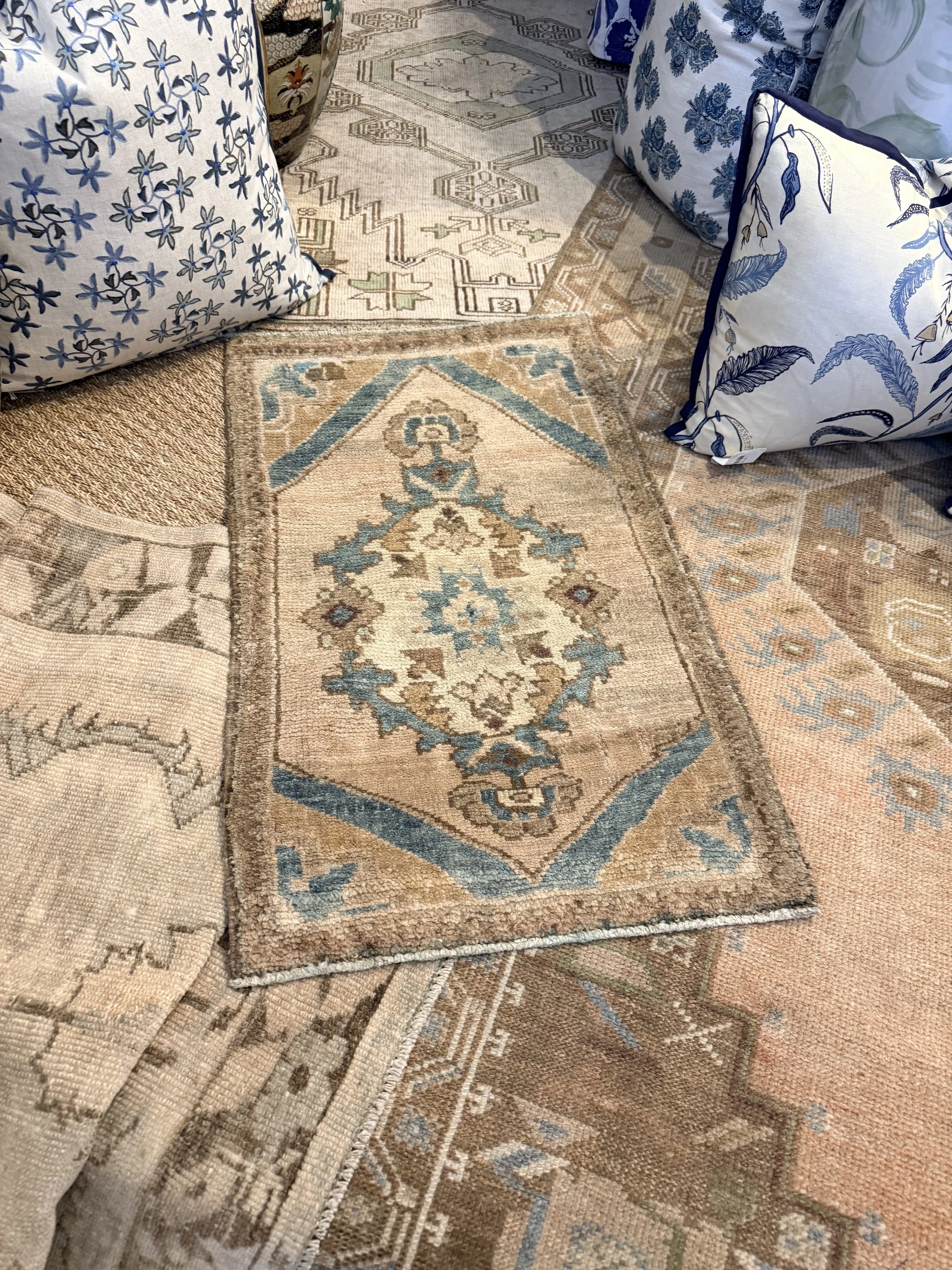 Close-up view of several overlapping vintage patterned area rugs and pillows with floral and geometric designs in shades of beige, blue, and tan.