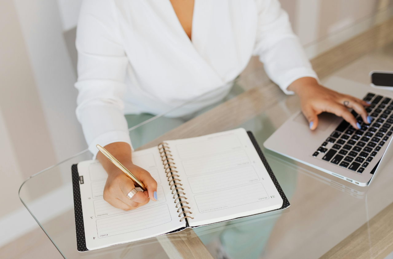 Woman's hand on desk with laptop and calendar planner representing professional travel preparation.
