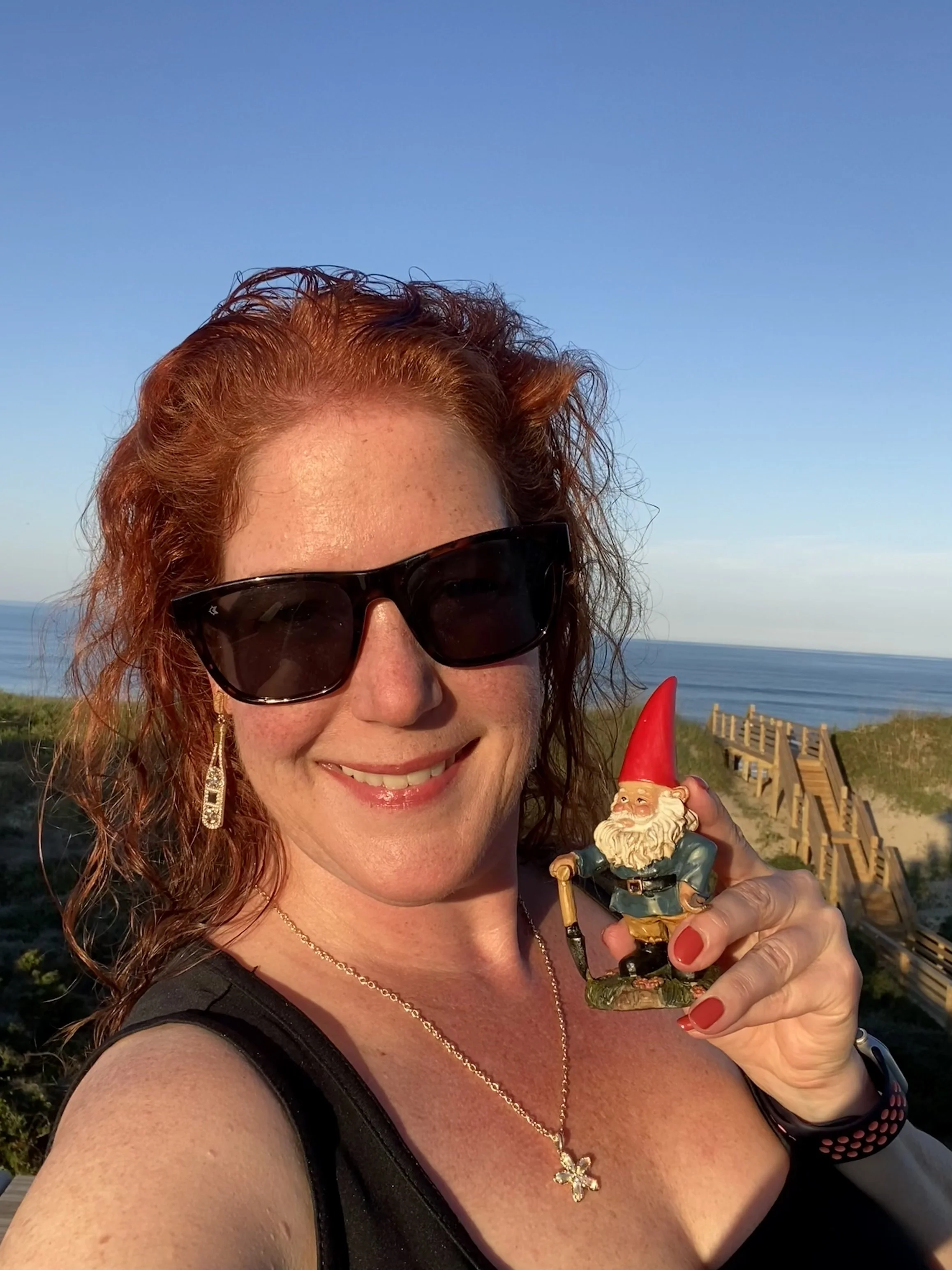 Amanda Bacqué holding her traveling gnome Louis at the Outer Banks North Carolina with the Atlantic Ocean in the background September 2025.