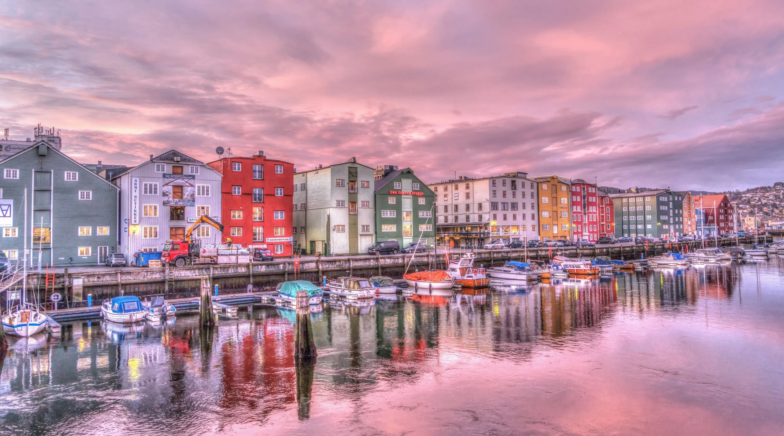 Colorful Scandinavian buildings along a harbor with boats docked in calm water and a pink and purple sky at sunset.