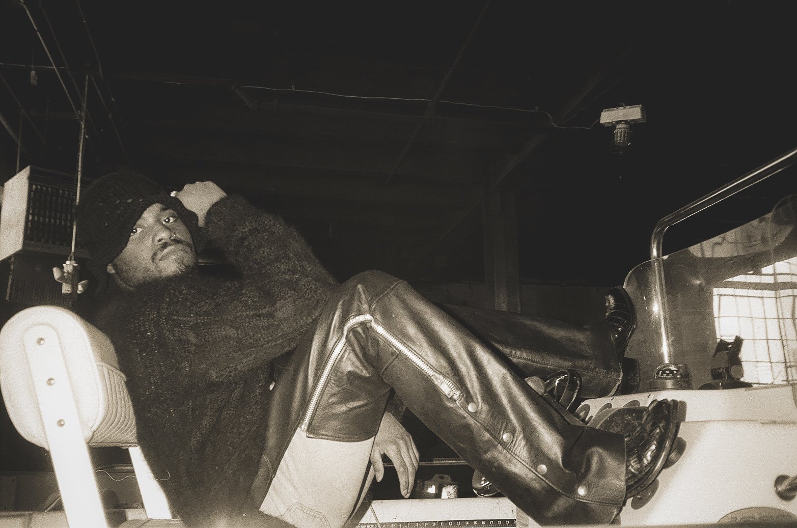 A person lying on a medical chair in a clinical setting, wearing a knit hat, warm sweater, and leather pants, with a machine or device nearby.