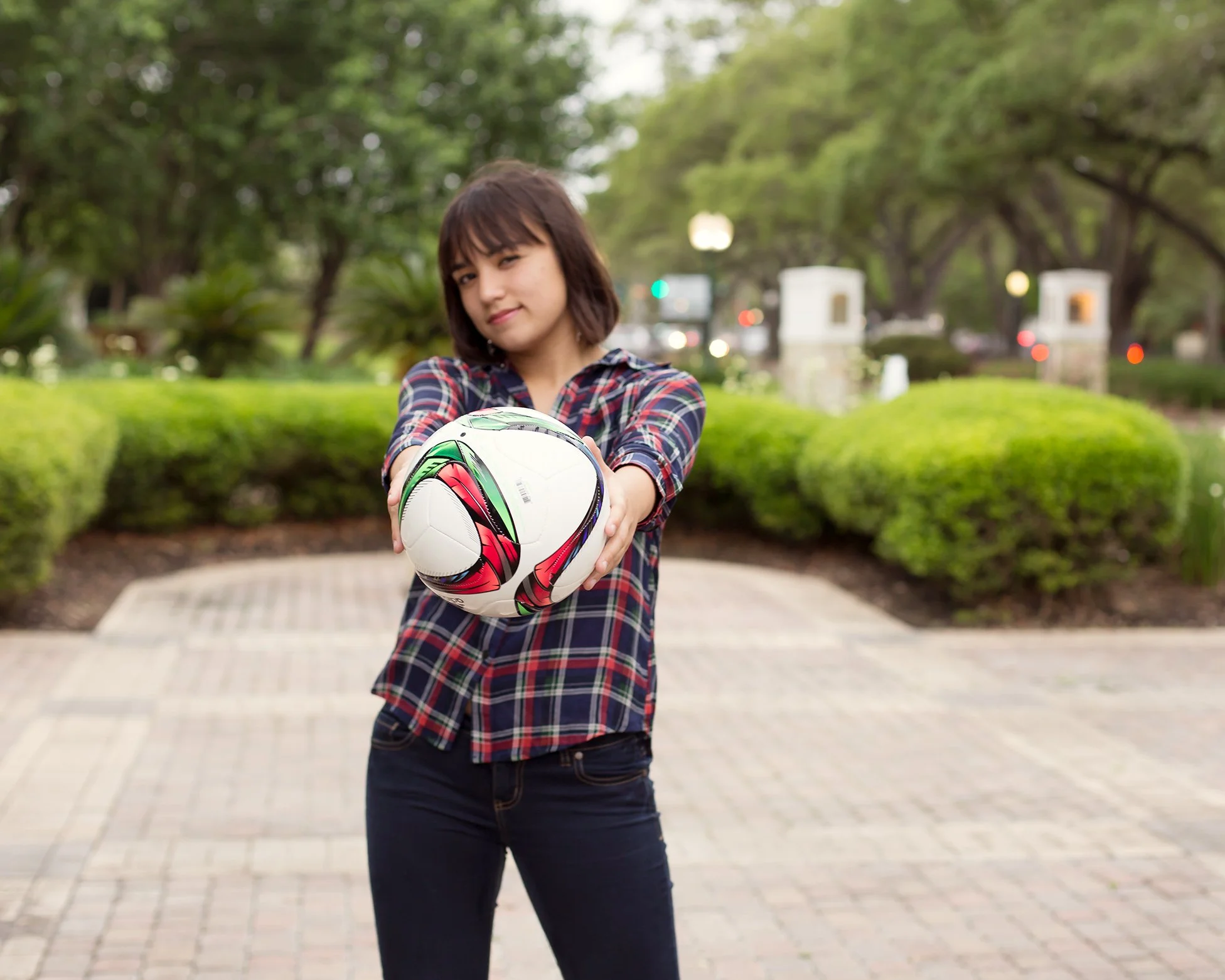Woman holding a soccer ball on a tree-lined park walkway