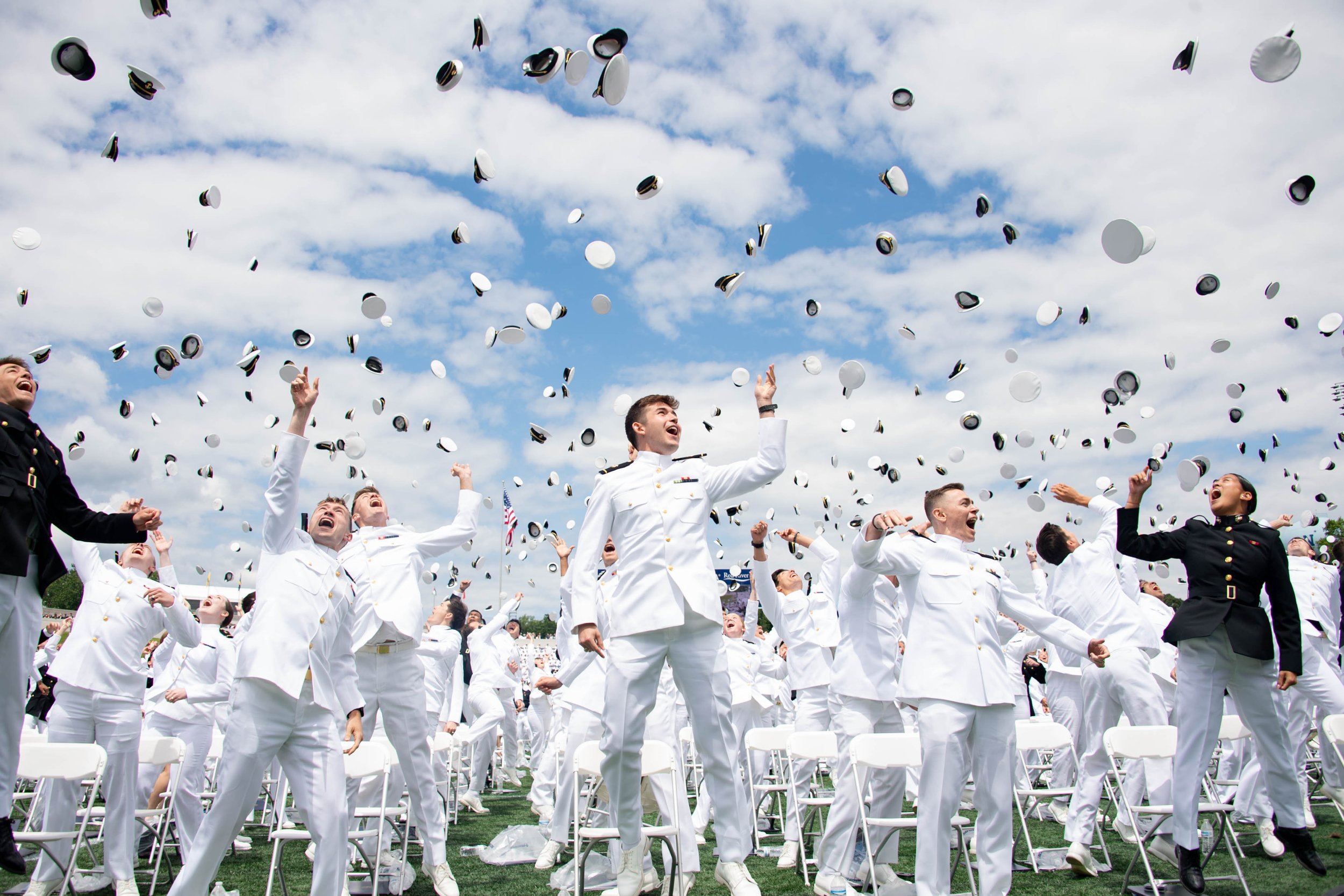 U.S. Naval Academy graduates celebrating as white and black military caps fly through the sky