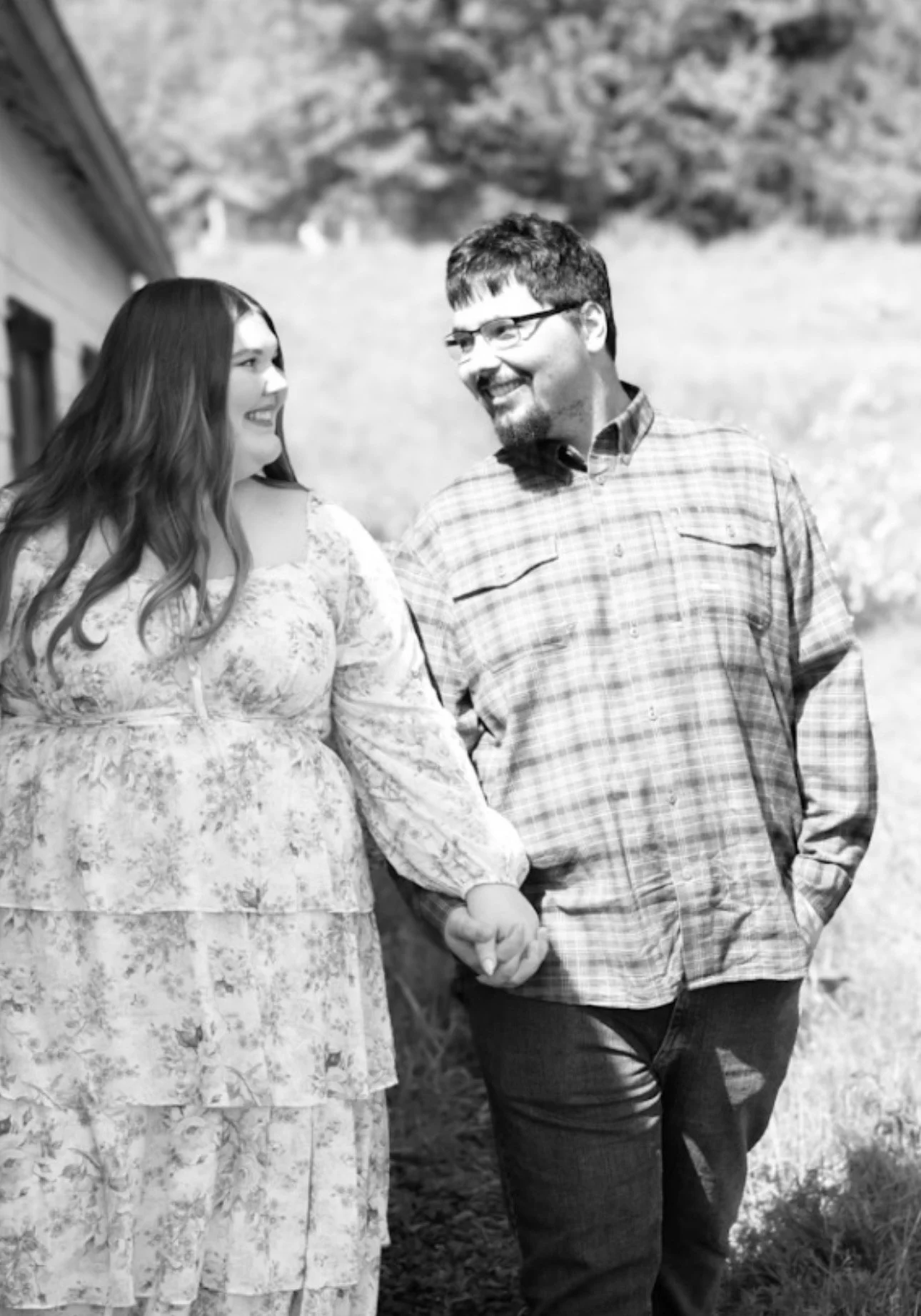 A smiling man and woman holding hands outdoors in a rural setting.