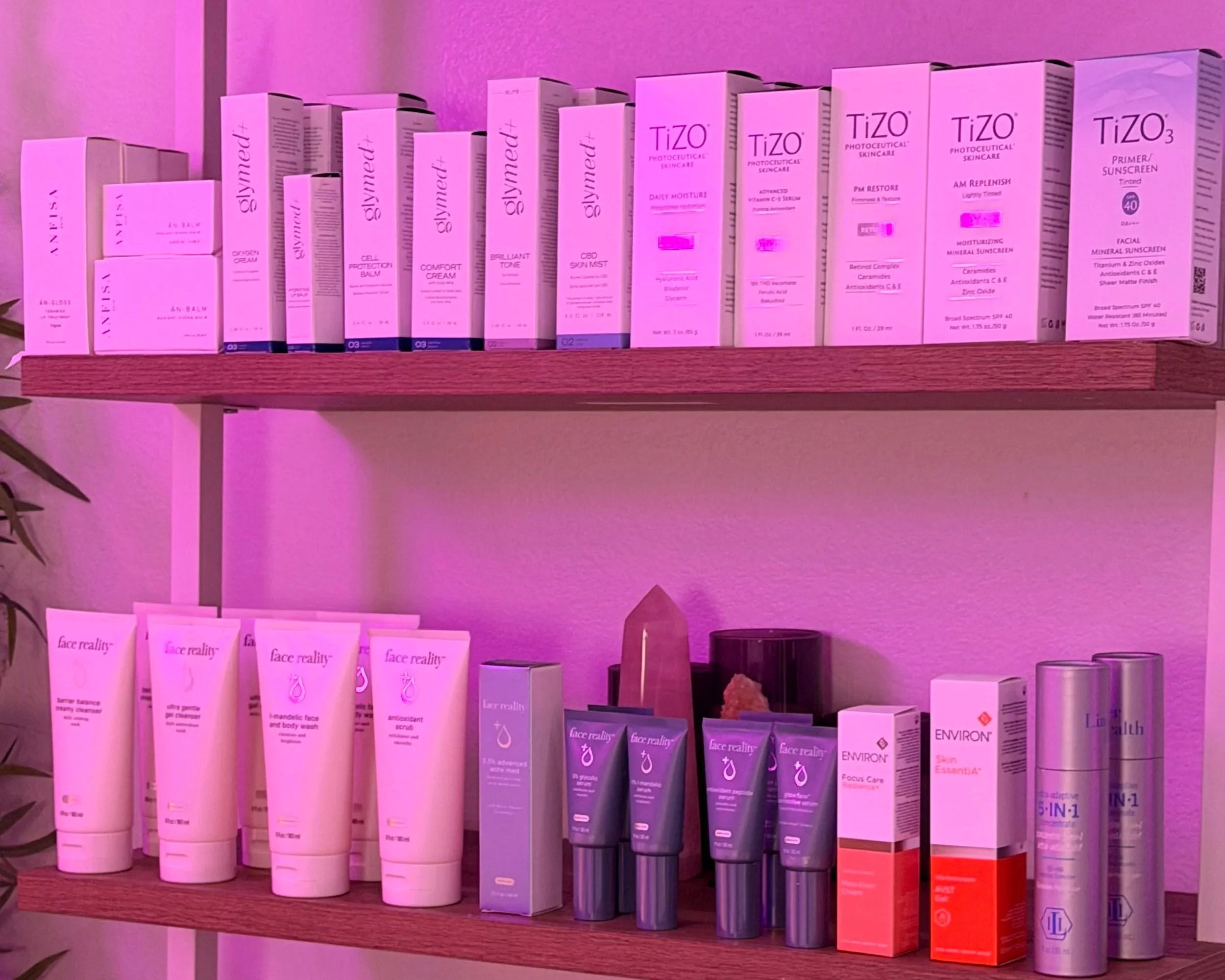 Shelves stocked with skincare and skincare-related products, mainly in pink and purple packaging, under pink lighting.