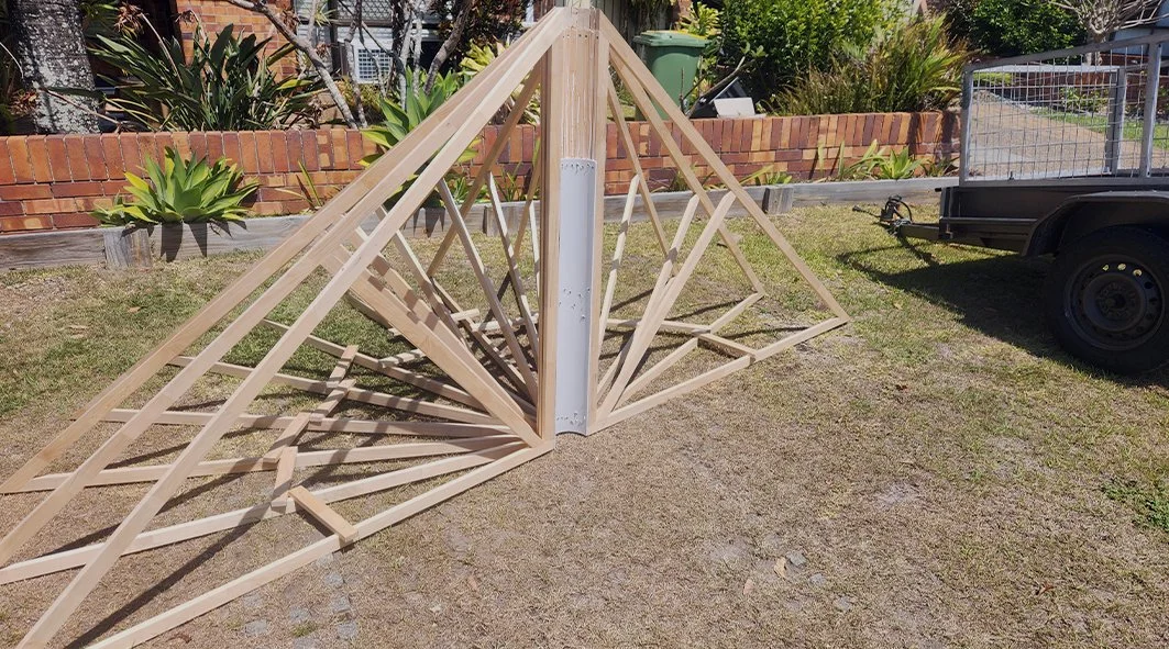 Two wooden triangular structures leaning against a metal pole in a yard.