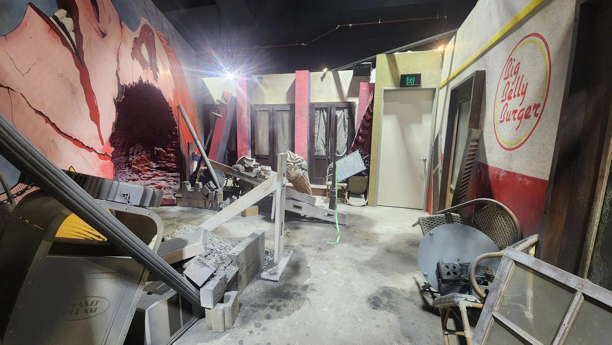 Interior of a restaurant under renovation or construction with debris, chairs, and equipment scattered around, a mural of a world map painted on the wall, and a sign that reads "Big Belly Burger."