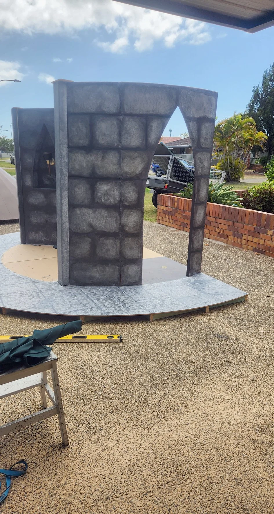 A structure resembling a stone archway with a medieval castle aesthetic, made of painted panels with a stone pattern, placed outdoors on a curved platform.