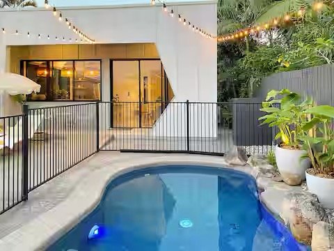 New modern cottage, magnesium pool, potted plants, festoon lighting, day beds, tropical surrounds. House with large glass doors beside pool.  Caloundra Sunshine Coast, Australia.