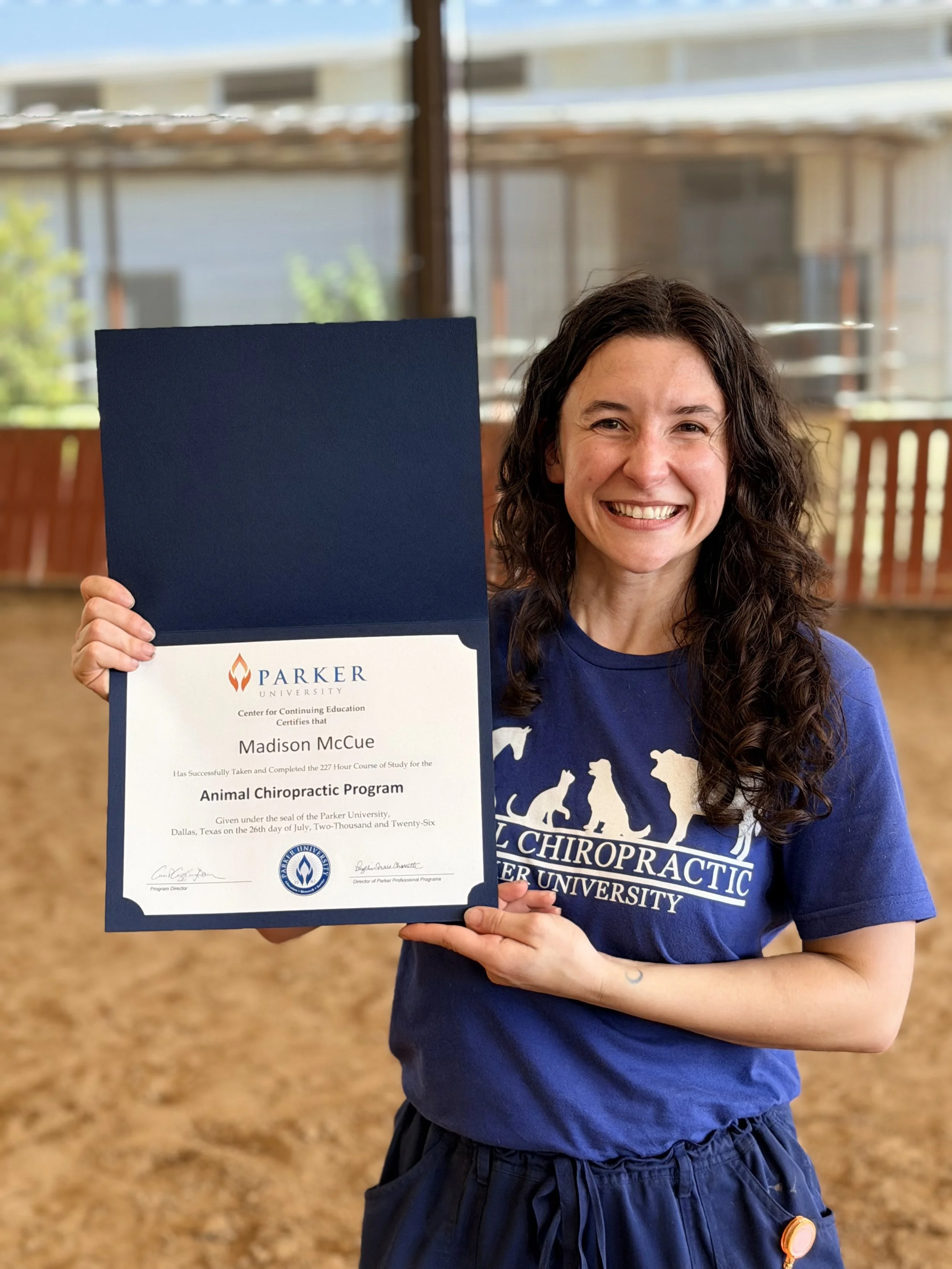 Dr. McCue, DC, holding her animal chiropractic graduate diploma from Parker University, highlighting specialized animal chiropractic training in dog chiropractic, cat chiropractic, equine chiropractic, and animal chiropractic care in Dallas, TX.