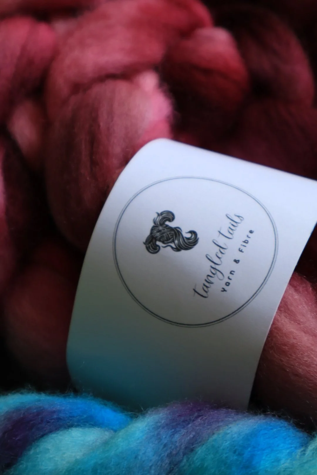 Close-up of a bundle of red yarn with a white tag labeled "Tangled Tail, born & fiber" attached to it.