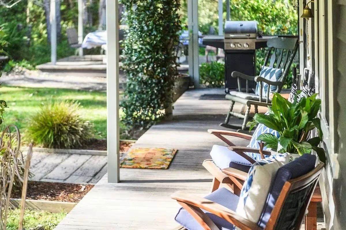 View of a covered porch with wooden chairs, outdoor plants, and a barbecue grill.