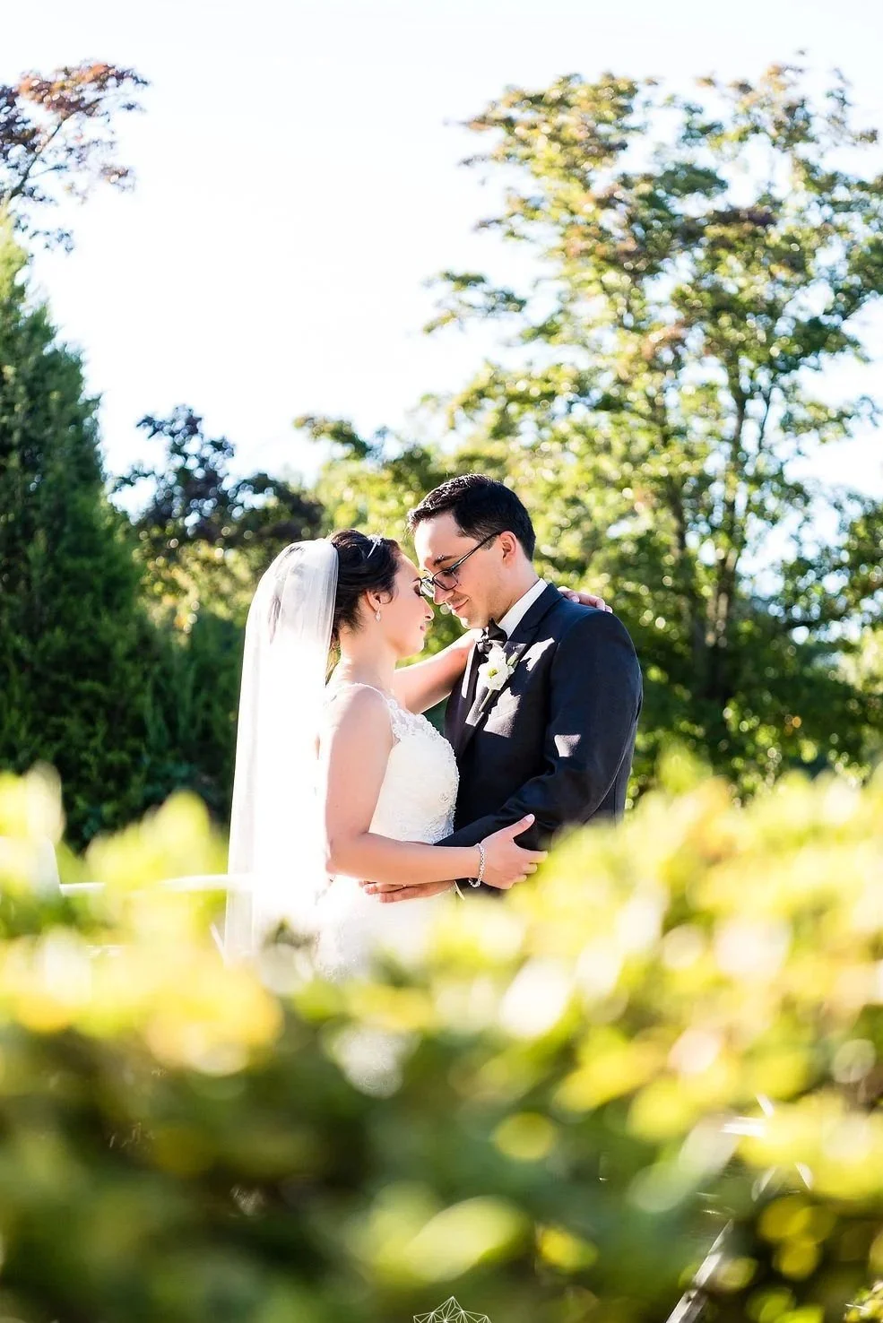 Bride and groom embracing outdoors in a sunlit garden on their wedding day.