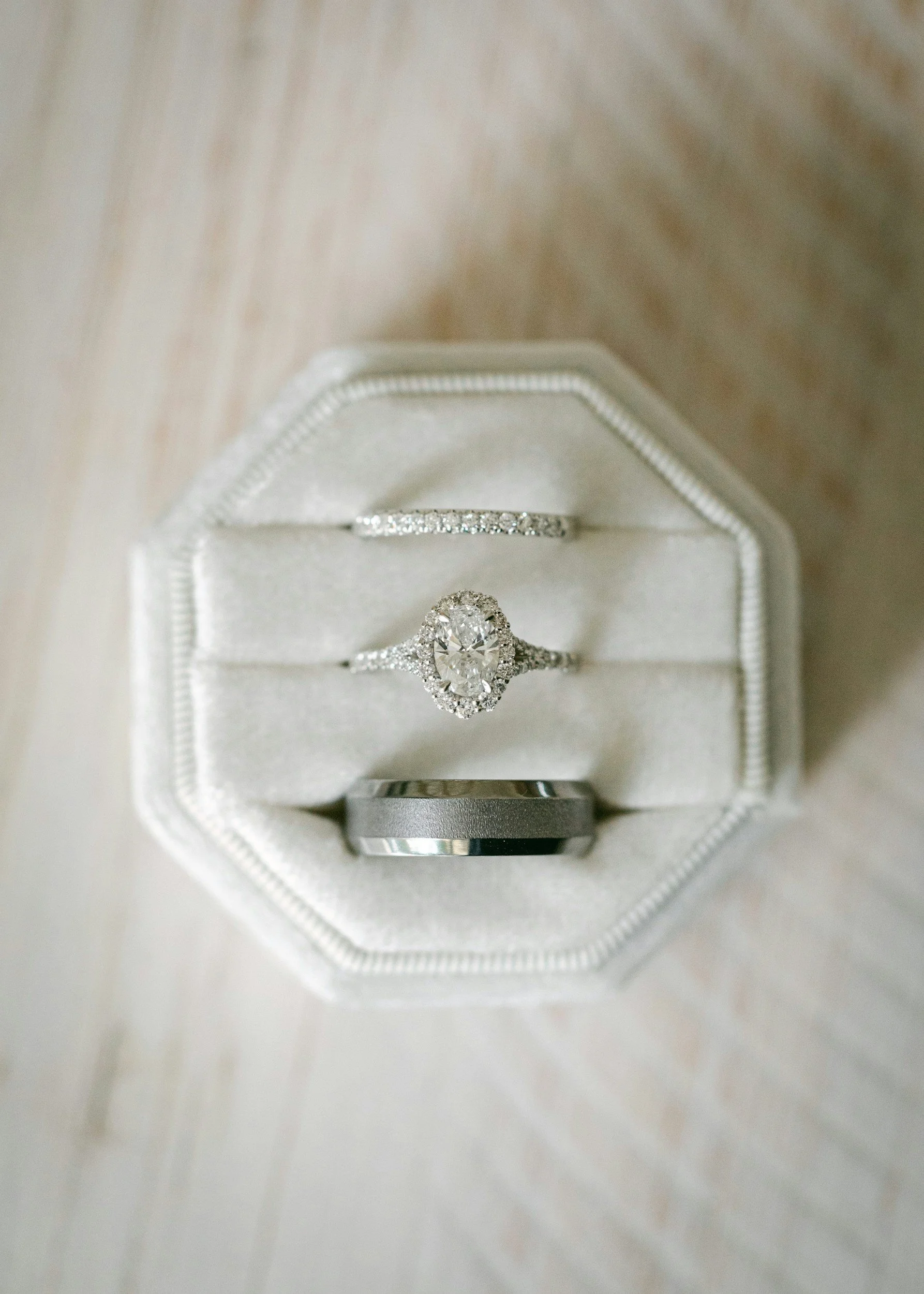 Engagement ring and wedding bands displayed in a white velvet ring box.