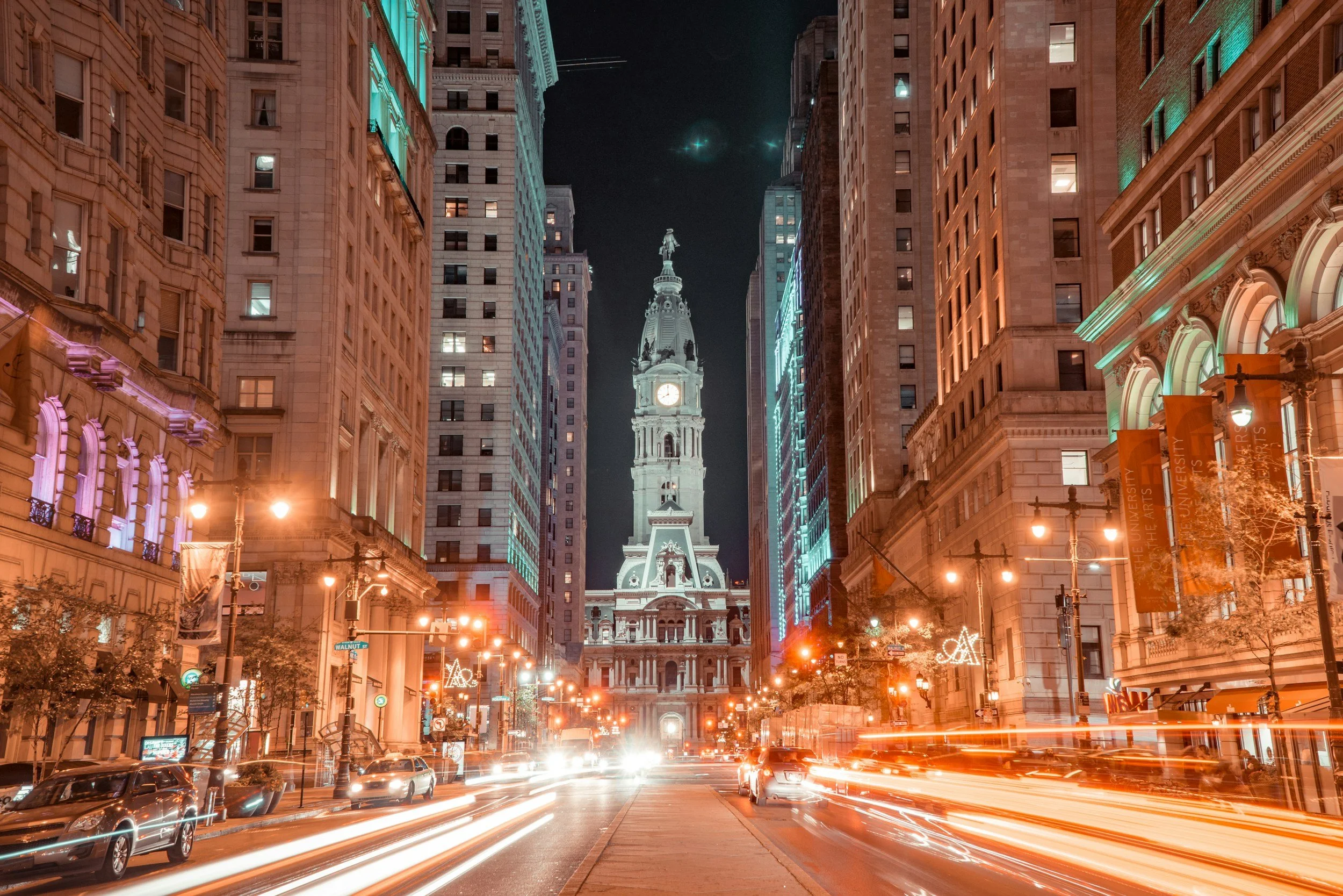 Philadelphia City Hall illuminated at night, framed by downtown buildings and city lights.