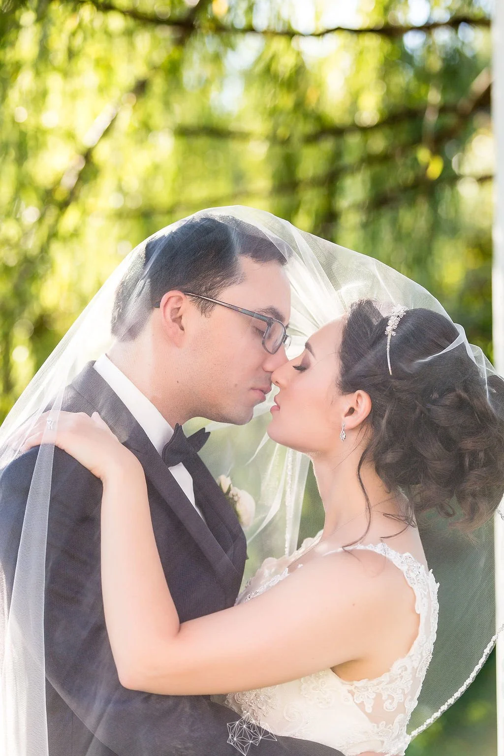 Bride and groom embracing under the bride’s veil during an outdoor wedding portrait.