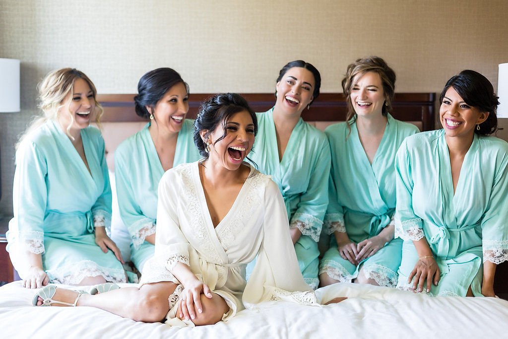 Bride and bridesmaids laughing together in matching robes while getting ready for the wedding.