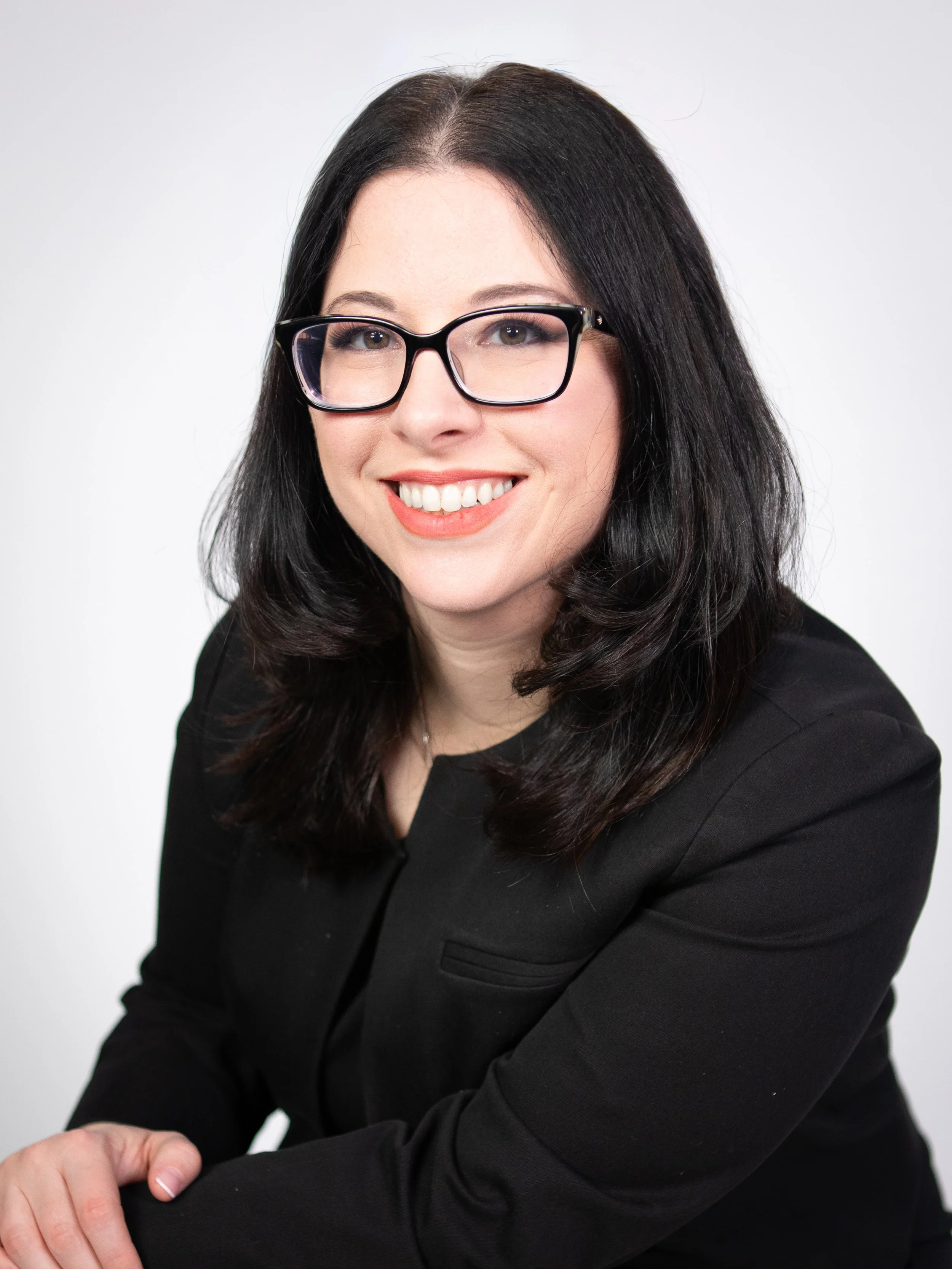 Professional headshot of Kiersten, the creative director, wearing black glasses and a black blazer.