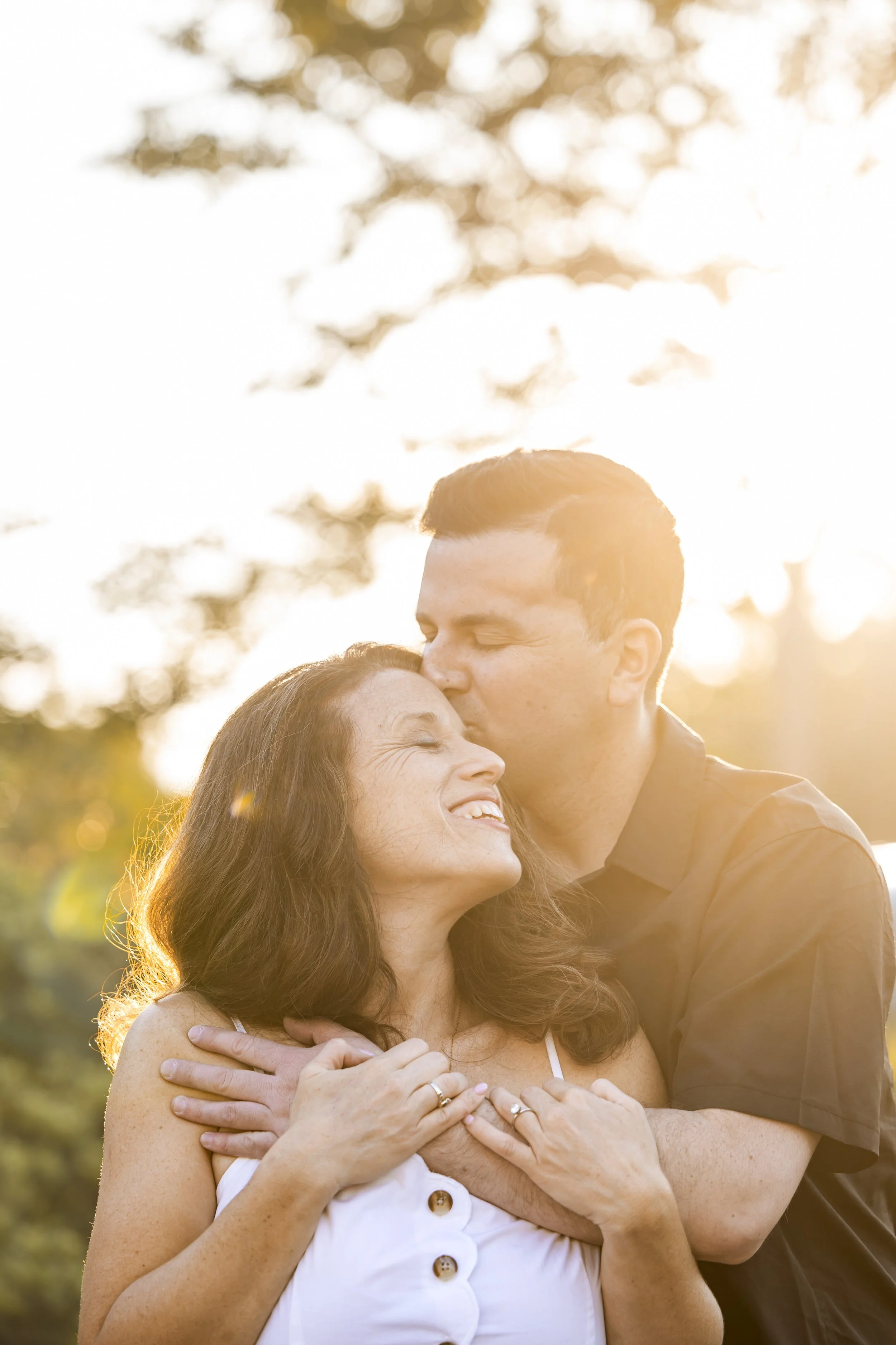 Couple embracing at sunset as the man kisses the woman on the forehead.