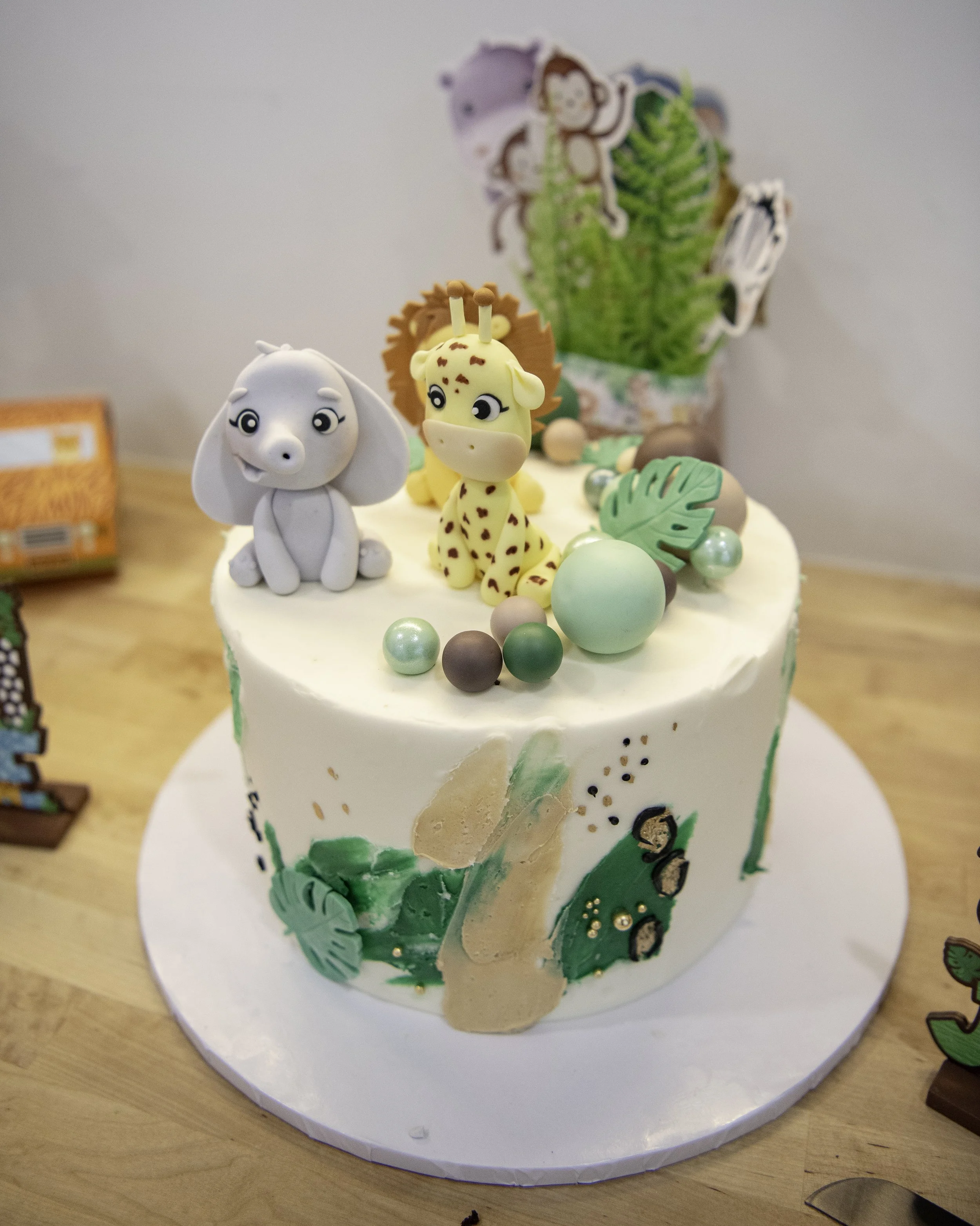 Jungle-themed celebration cake decorated with fondant elephant, giraffe, and tropical details.