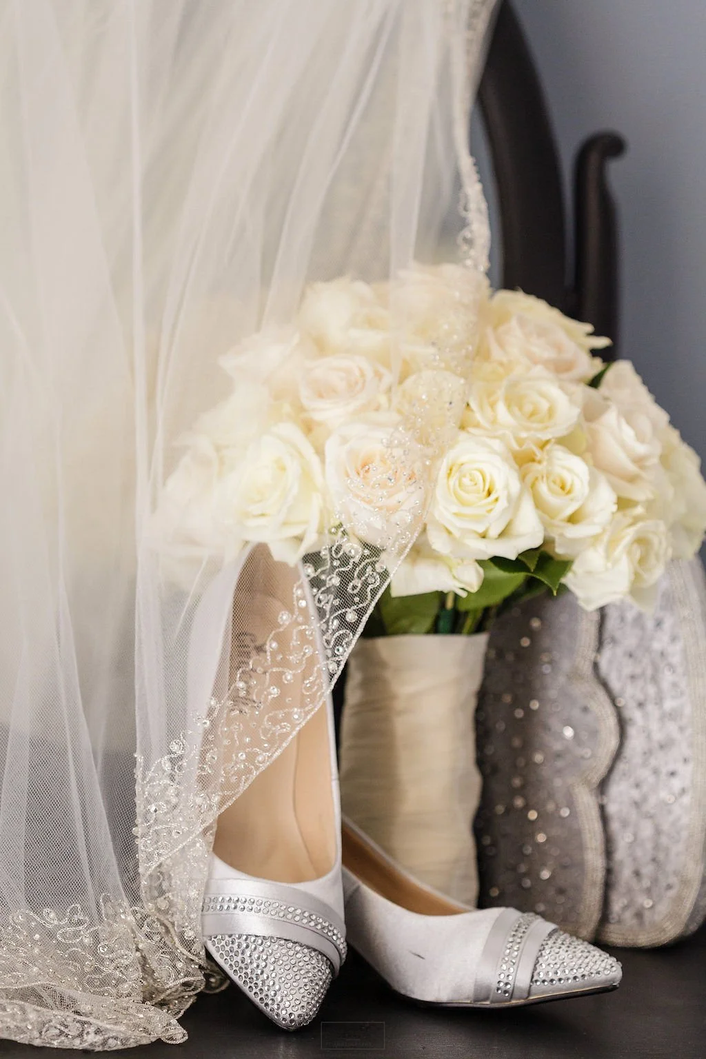 White bridal shoes, wedding veil, and bouquet of white roses arranged together.