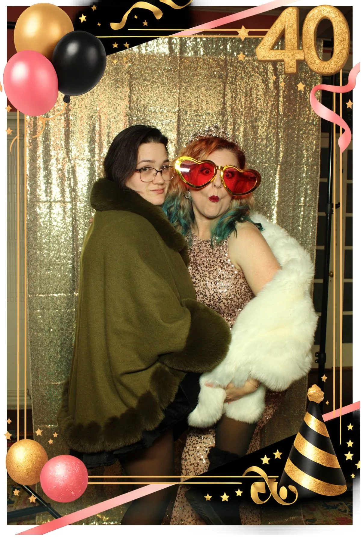 Two women posing in festive outfits and oversized glasses at a 40th birthday photo booth.
