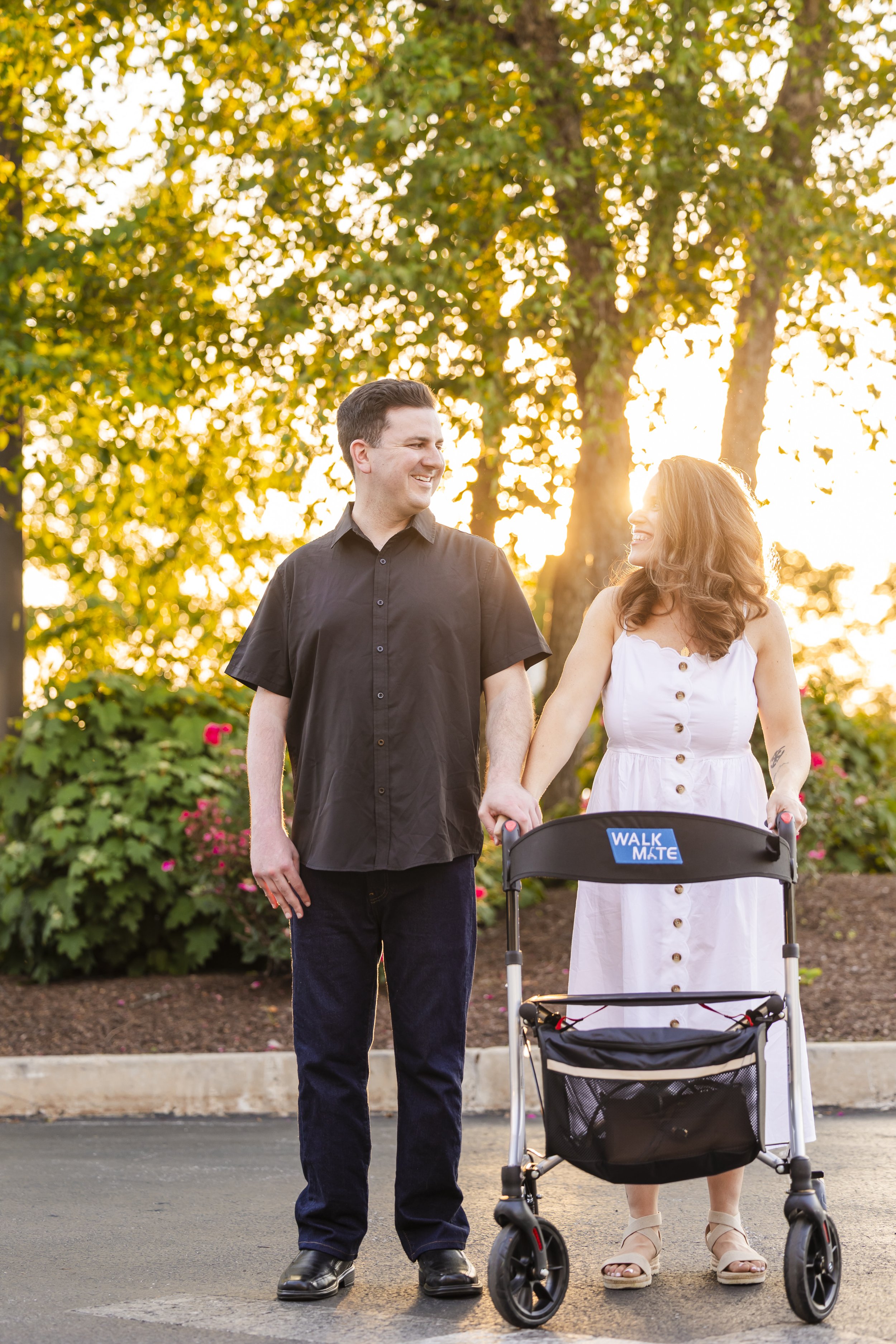 Couple holding hands outdoors at sunset while walking with a mobility walker.