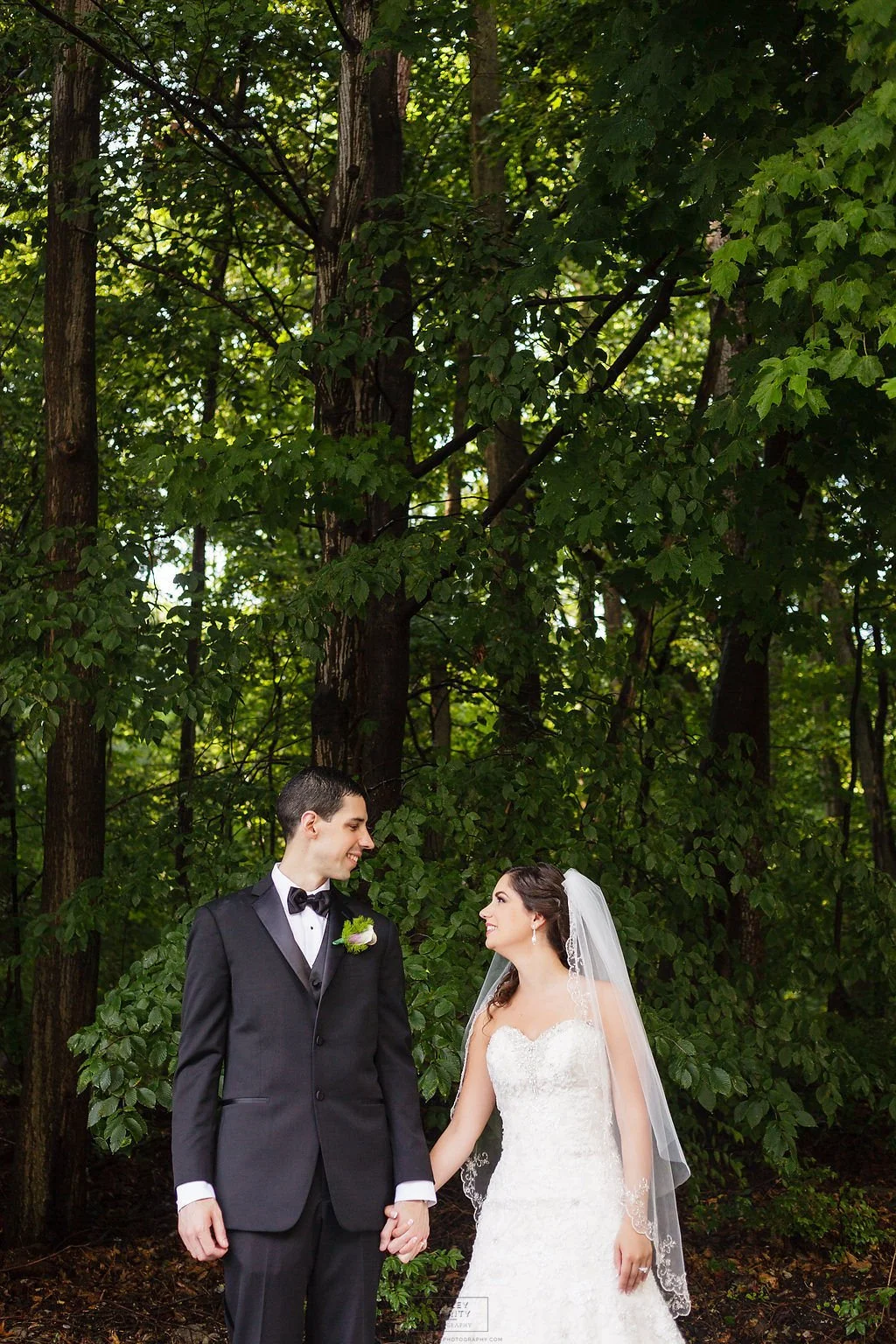 Bride and groom holding hands and looking at each other during an outdoor wedding portrait.