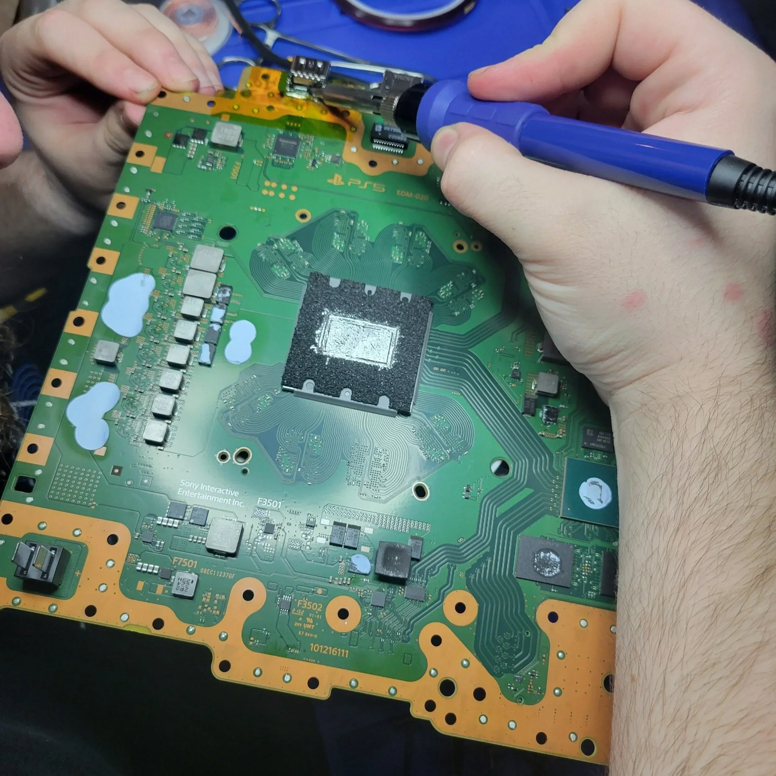 Hands working on a circuit board with a soldering tool and various electronic components.