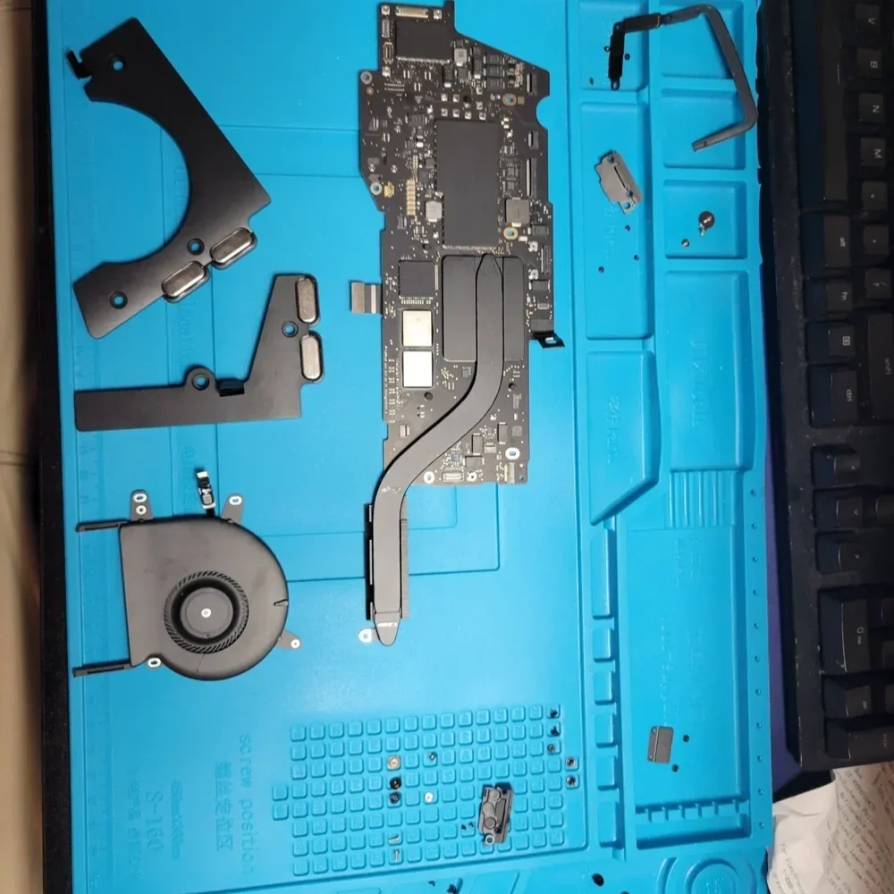 Disassembled laptop components laid out on a blue anti-static mat, including a motherboard, cooling fan, and other small parts.