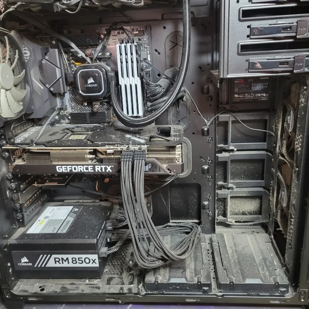 Dirt and dust inside a computer case with multiple cables, a graphics card labeled NVIDIA GeForce RTX, a power supply labeled RM850x, a CPU cooler, and various empty drive bays.