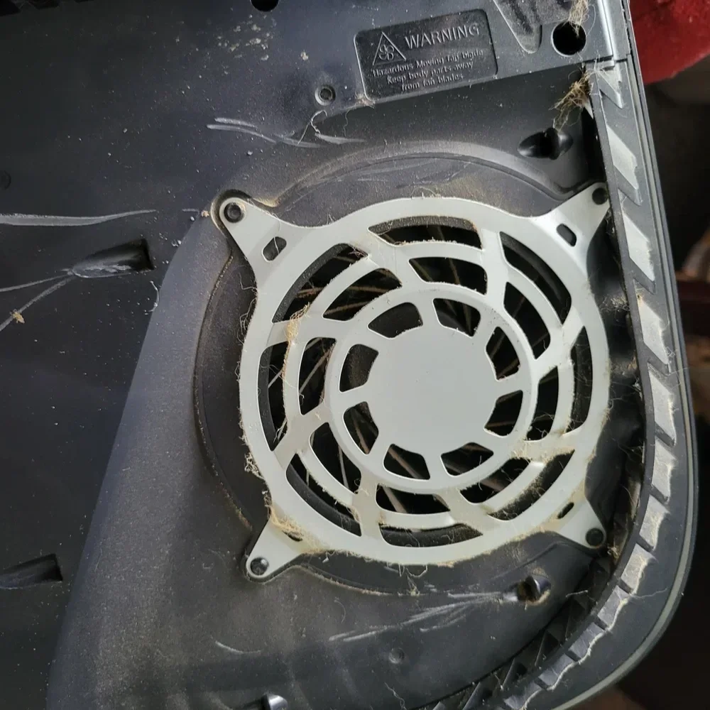 Inside of an electronic device, showing a black fan with dust and spider webs on it.